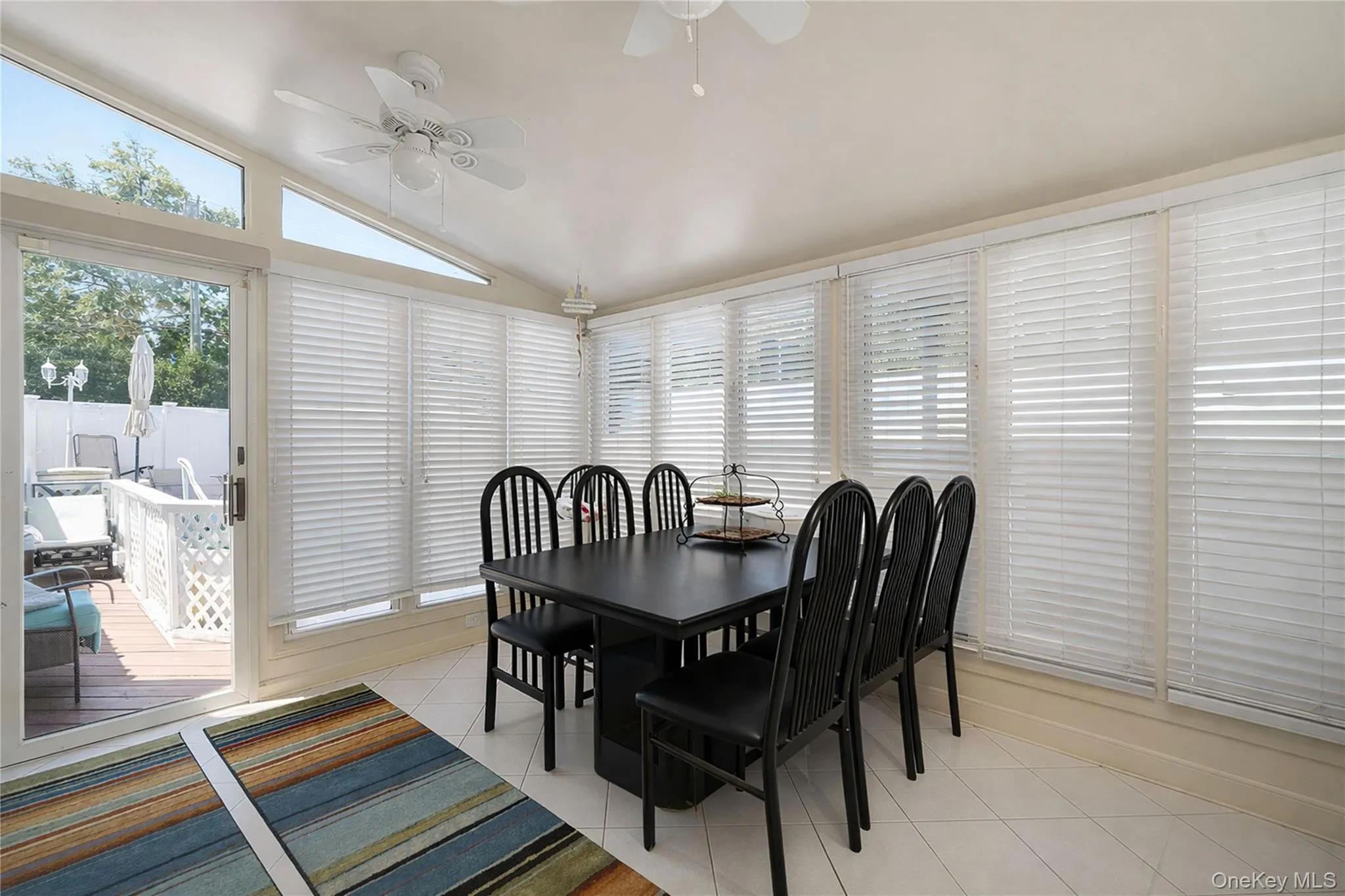 Sunroom featuring a vaulted ceiling with two ceiling fans, multiple windows with horizontal blinds, and tile flooring Sunroom featuring a vaulted ceiling with two ceiling fans, multiple windows with horizontal blinds, and tile flooring
