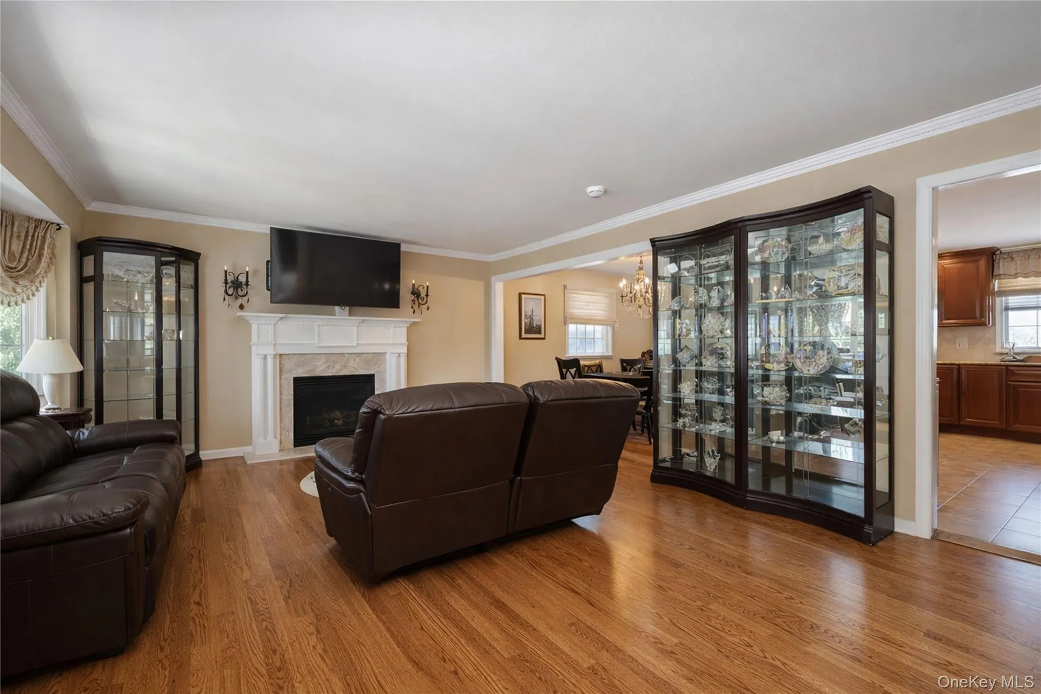 Living area featuring wood-finish flooring, crown molding, and a fireplace with a stone surround and white mantel Living area featuring wood-finish flooring, crown molding, and a fireplace with a stone surround and white mantel