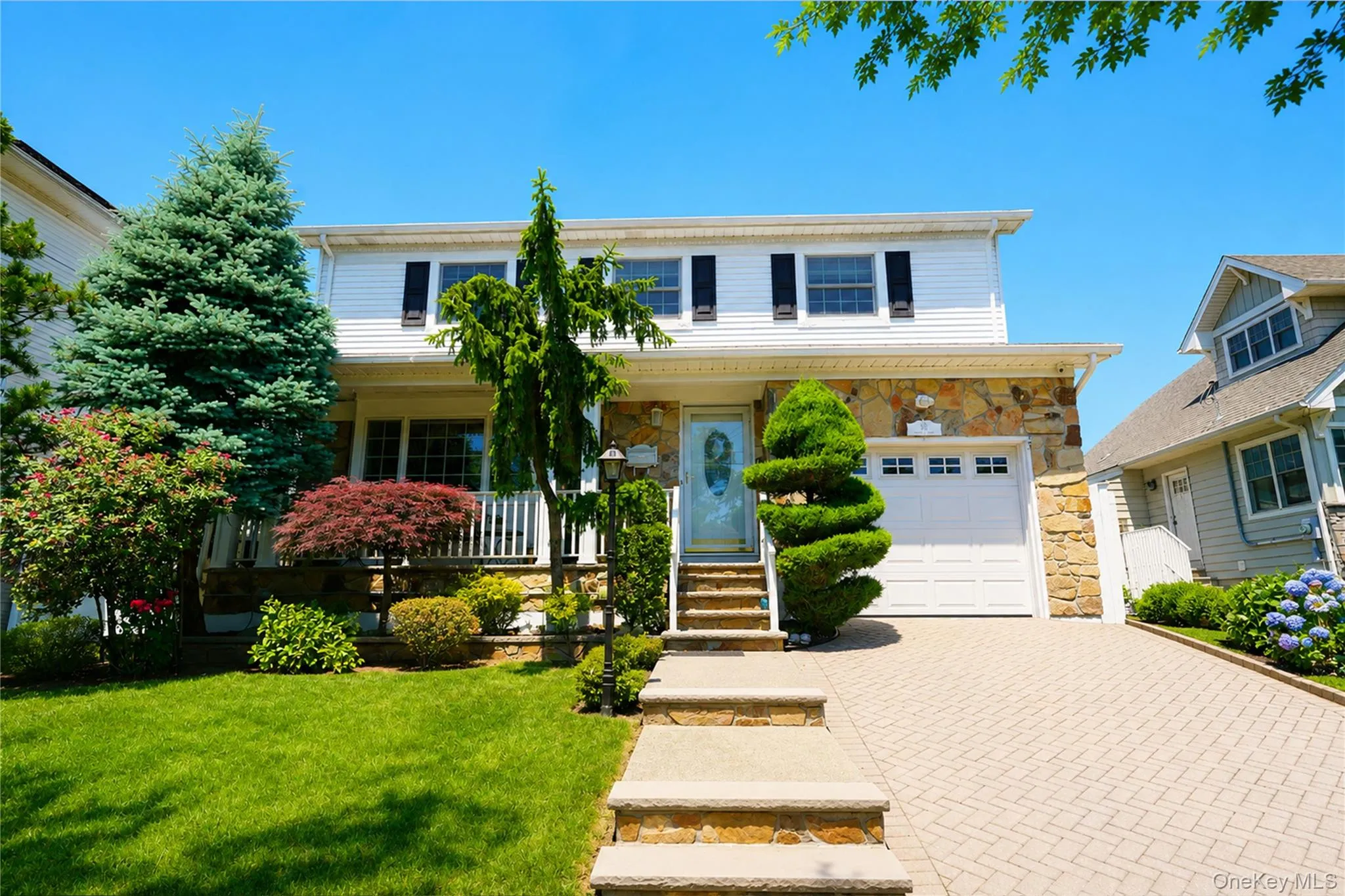 Two-story residence featuring white siding, stone façade accents, and a paved driveway Two-story residence featuring white siding, stone façade accents, and a paved driveway