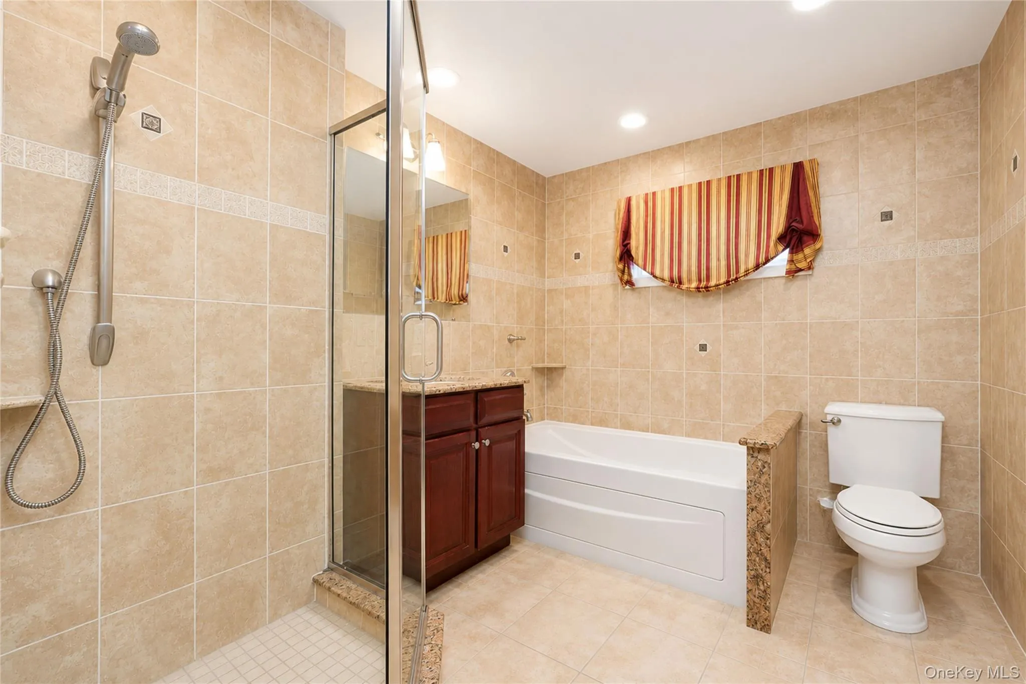Tiled bathroom featuring a glass-enclosed shower, a separate soaking tub, a dark wood vanity with a stone countertop, and recessed lighting Tiled bathroom featuring a glass-enclosed shower, a separate soaking tub, a dark wood vanity with a stone countertop, and recessed lighting