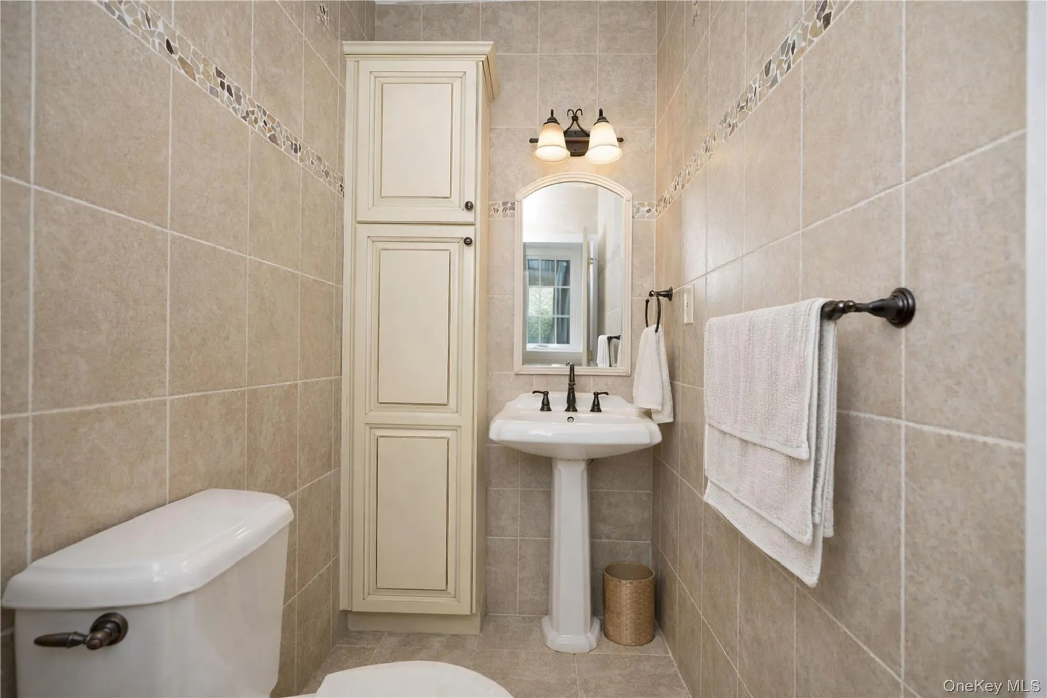 Pedestal sink with dark-finished faucet, illuminated by a three-light vanity fixture Pedestal sink with dark-finished faucet, illuminated by a three-light vanity fixture