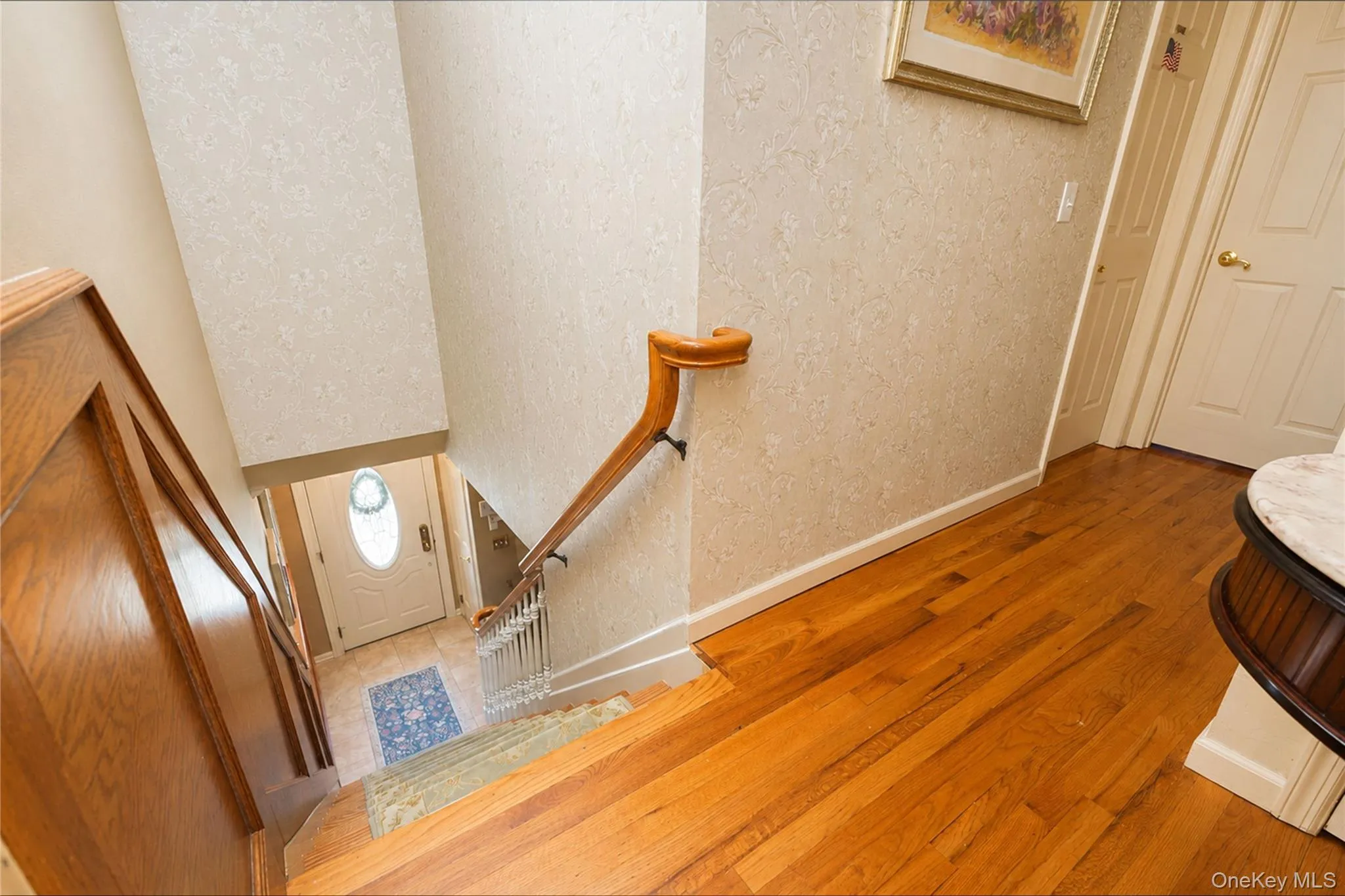 Hardwood flooring extending from the hallway, featuring a wooden staircase with a matching handrail and white balusters Hardwood flooring extending from the hallway, featuring a wooden staircase with a matching handrail and white balusters