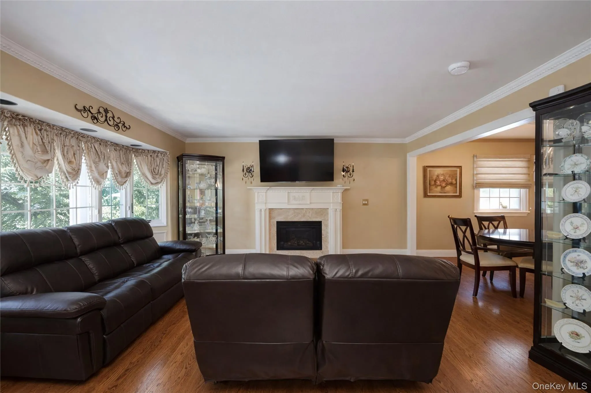 Living area featuring wood-finish flooring, a fireplace with a stone surround and mantel, and crown molding Living area featuring wood-finish flooring, a fireplace with a stone surround and mantel, and crown molding