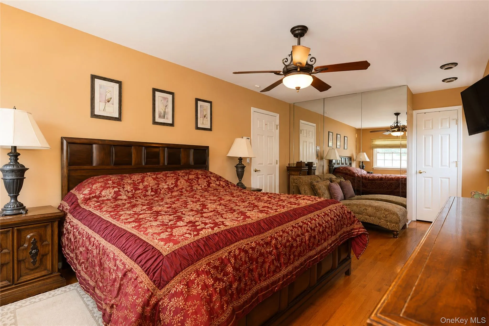 Spacious room featuring wood-finish flooring, a ceiling fan with light fixture, mirrored wall panels, white paneled doors, and recessed lighting Spacious room featuring wood-finish flooring, a ceiling fan with light fixture, mirrored wall panels, white paneled doors, and recessed lighting