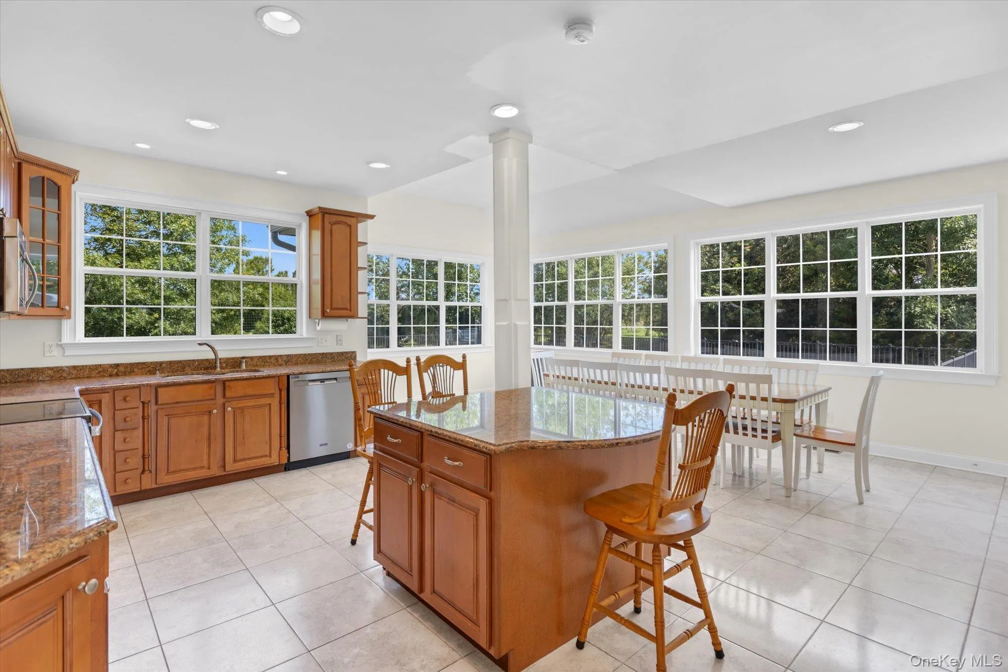 Open-concept kitchen with wood cabinetry, granite countertops, stainless steel dishwasher, a center island, and tile flooring Open-concept kitchen with wood cabinetry, granite countertops, stainless steel dishwasher, a center island, and tile flooring