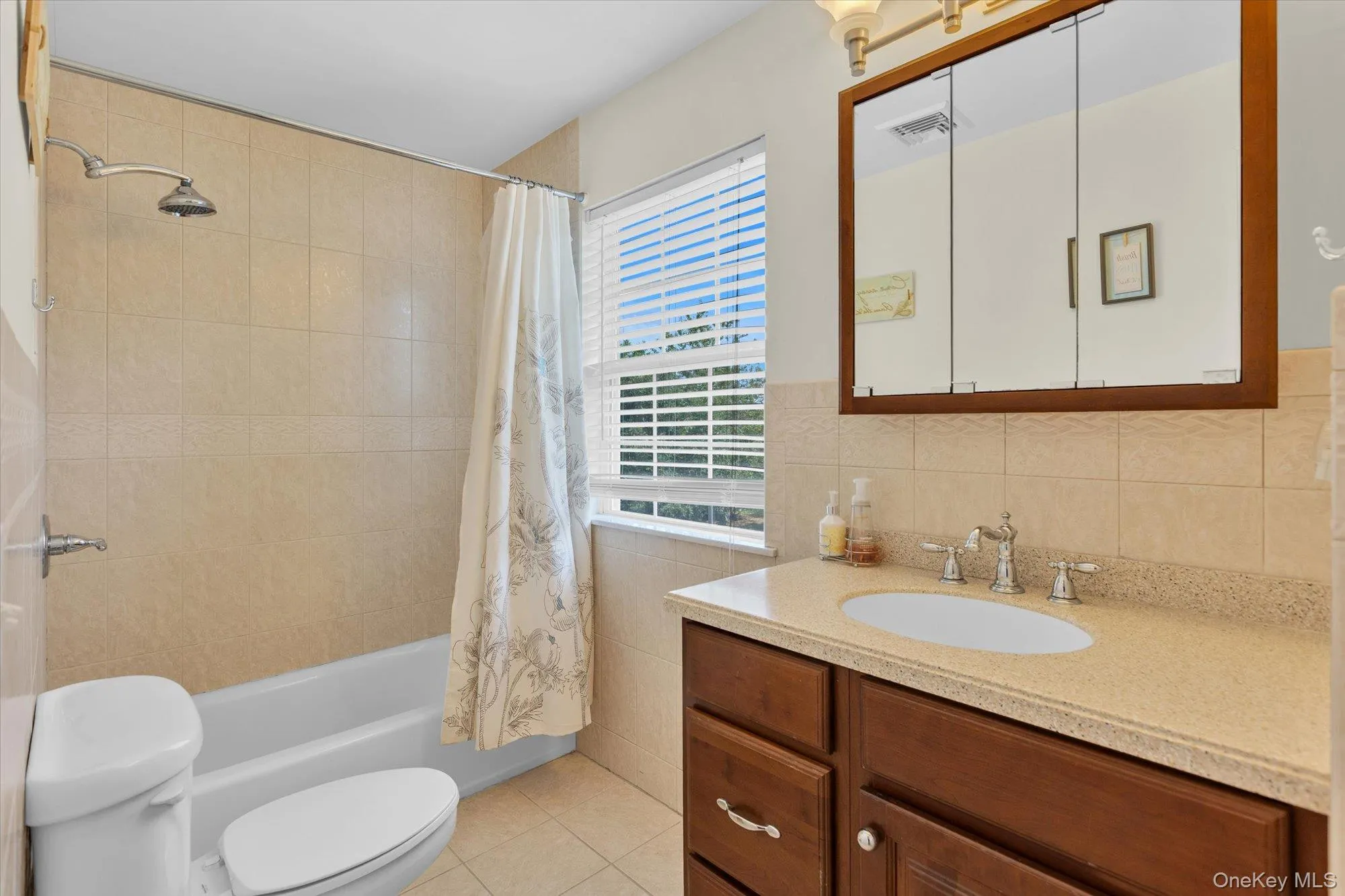 Bathroom featuring a built-in vanity and integrated sink, a tiled shower/tub combination, a window with blinds, and a mirrored medicine cabinet Bathroom featuring a built-in vanity and integrated sink, a tiled shower/tub combination, a window with blinds, and a mirrored medicine cabinet