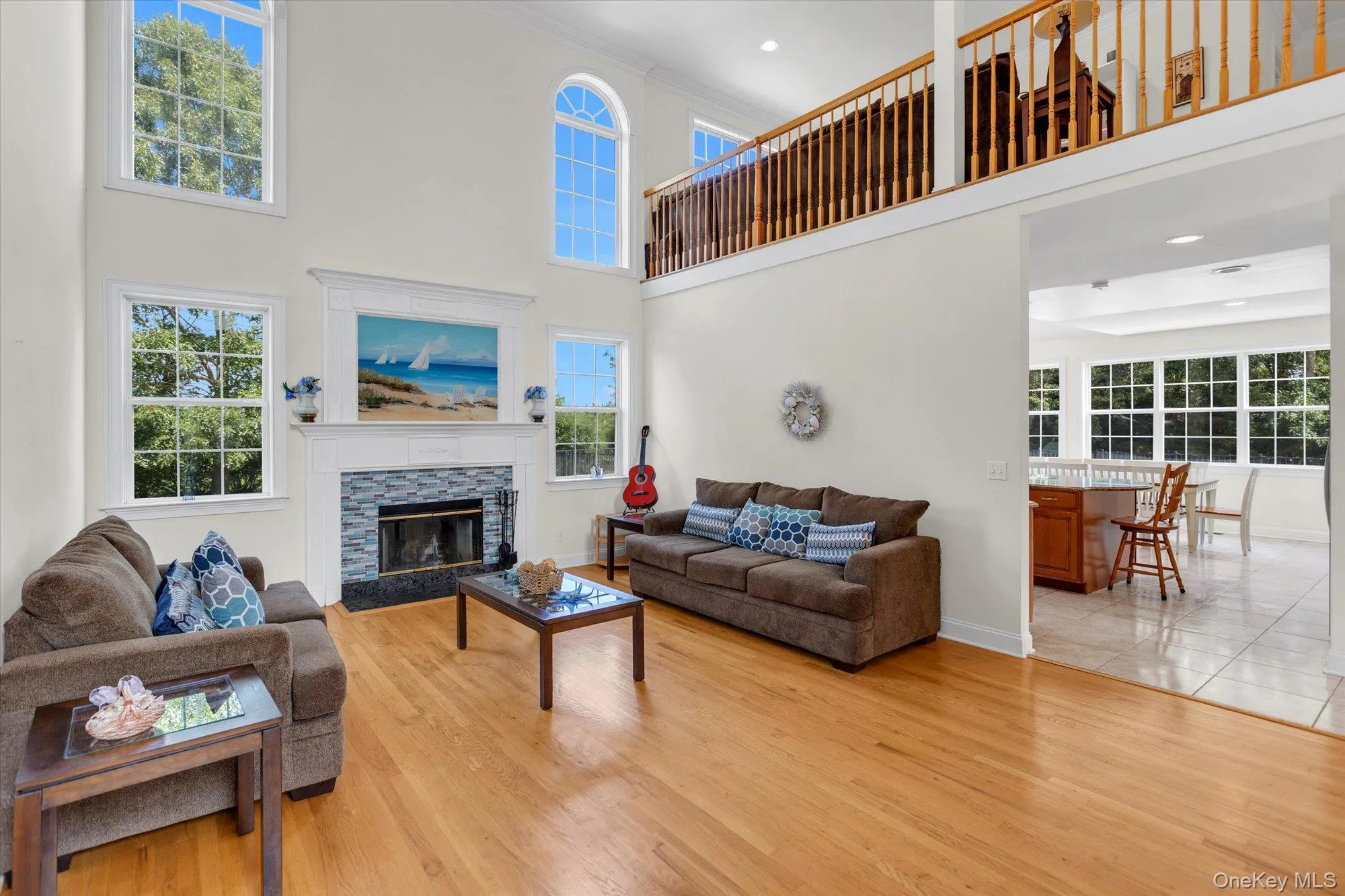 Two-story living area with hardwood flooring, a fireplace featuring a stone surround and hearth, and an upper-level railing overlooking the living room Two-story living area with hardwood flooring, a fireplace featuring a stone surround and hearth, and an upper-level railing overlooking the living room