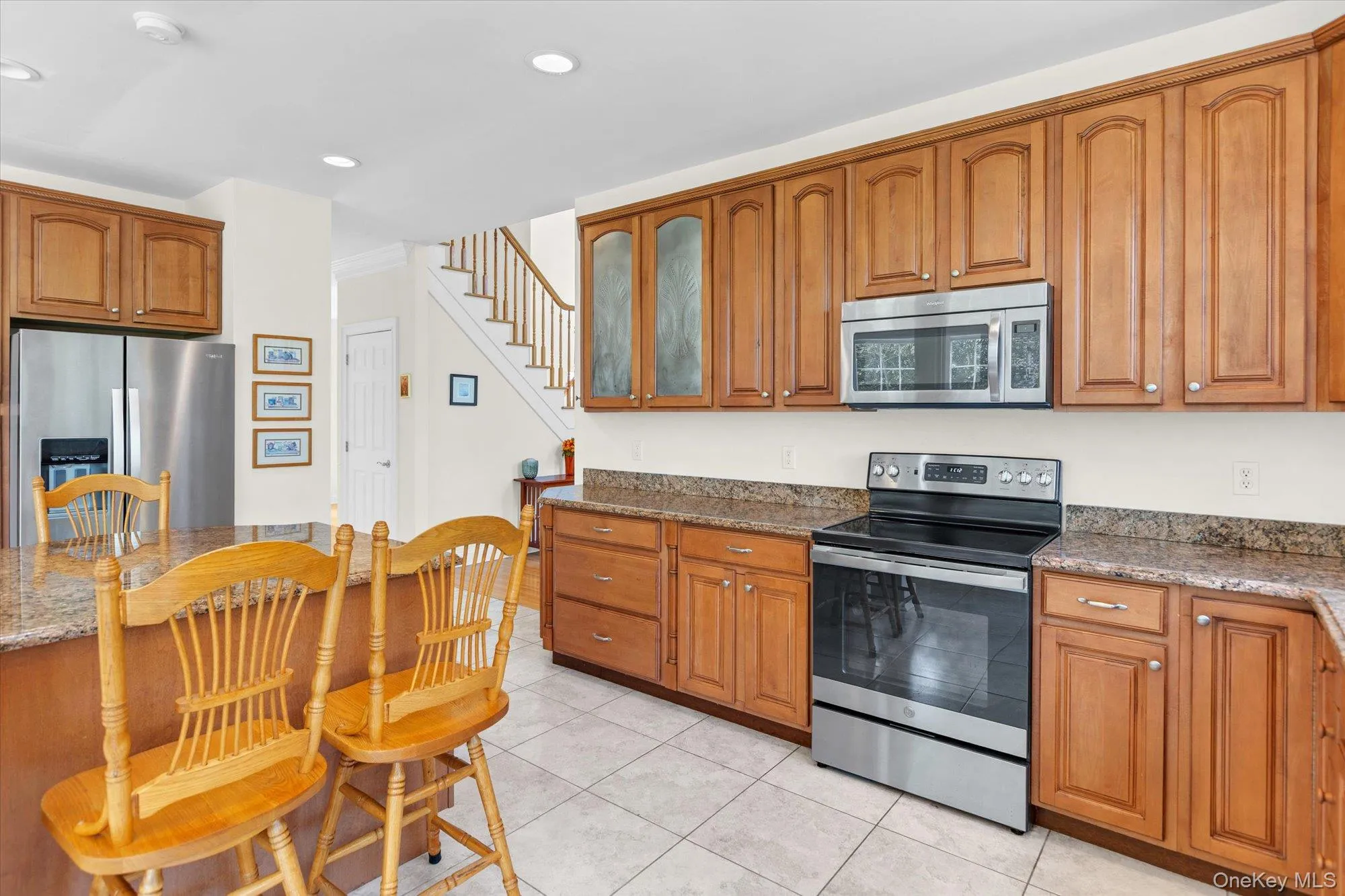 Kitchen featuring stainless steel appliances, wood cabinetry, granite-style countertops, and tile flooring Kitchen featuring stainless steel appliances, wood cabinetry, granite-style countertops, and tile flooring