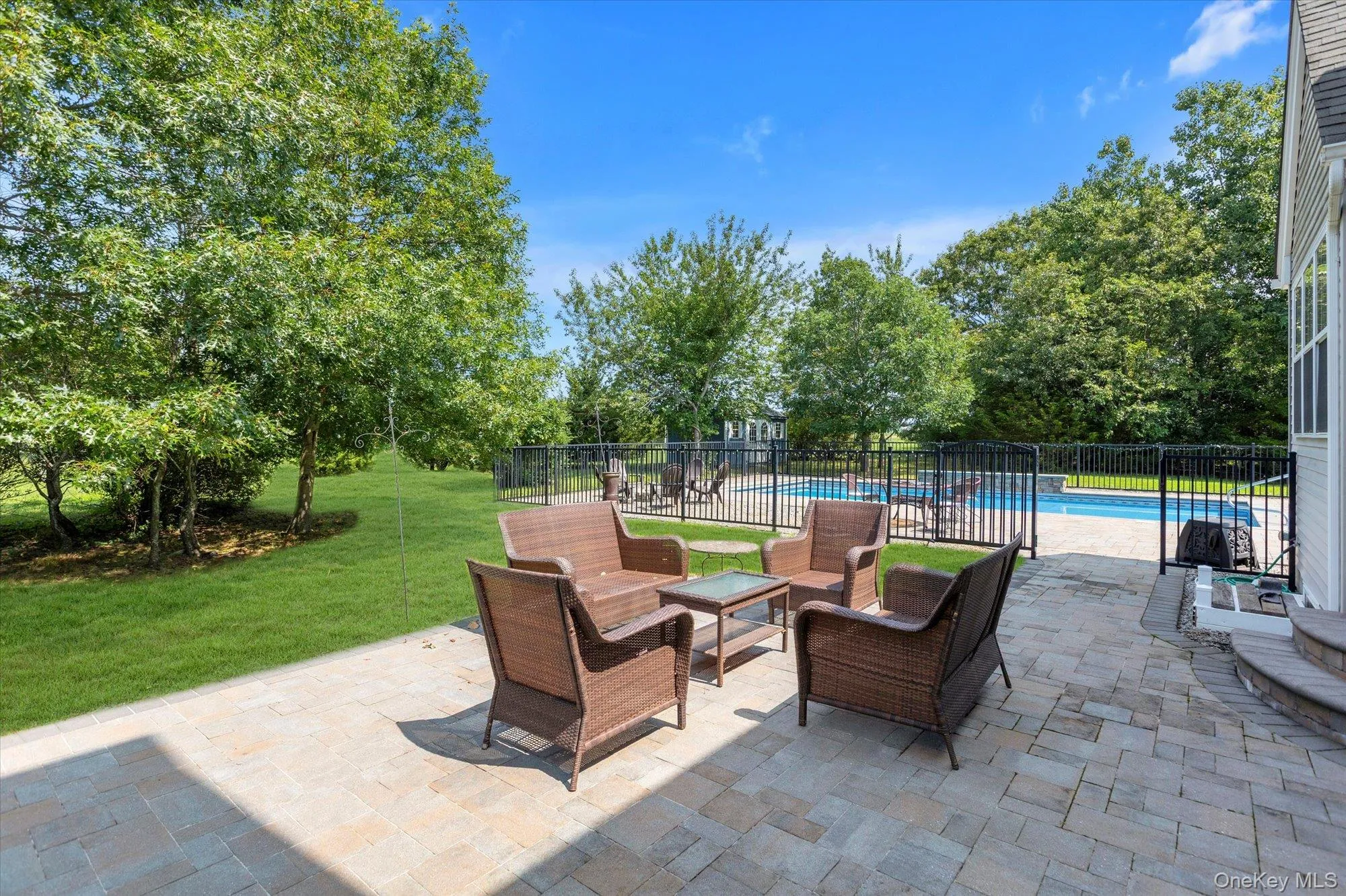 Paved stone patio with a fenced swimming pool, expansive lawn, and mature trees Paved stone patio with a fenced swimming pool, expansive lawn, and mature trees