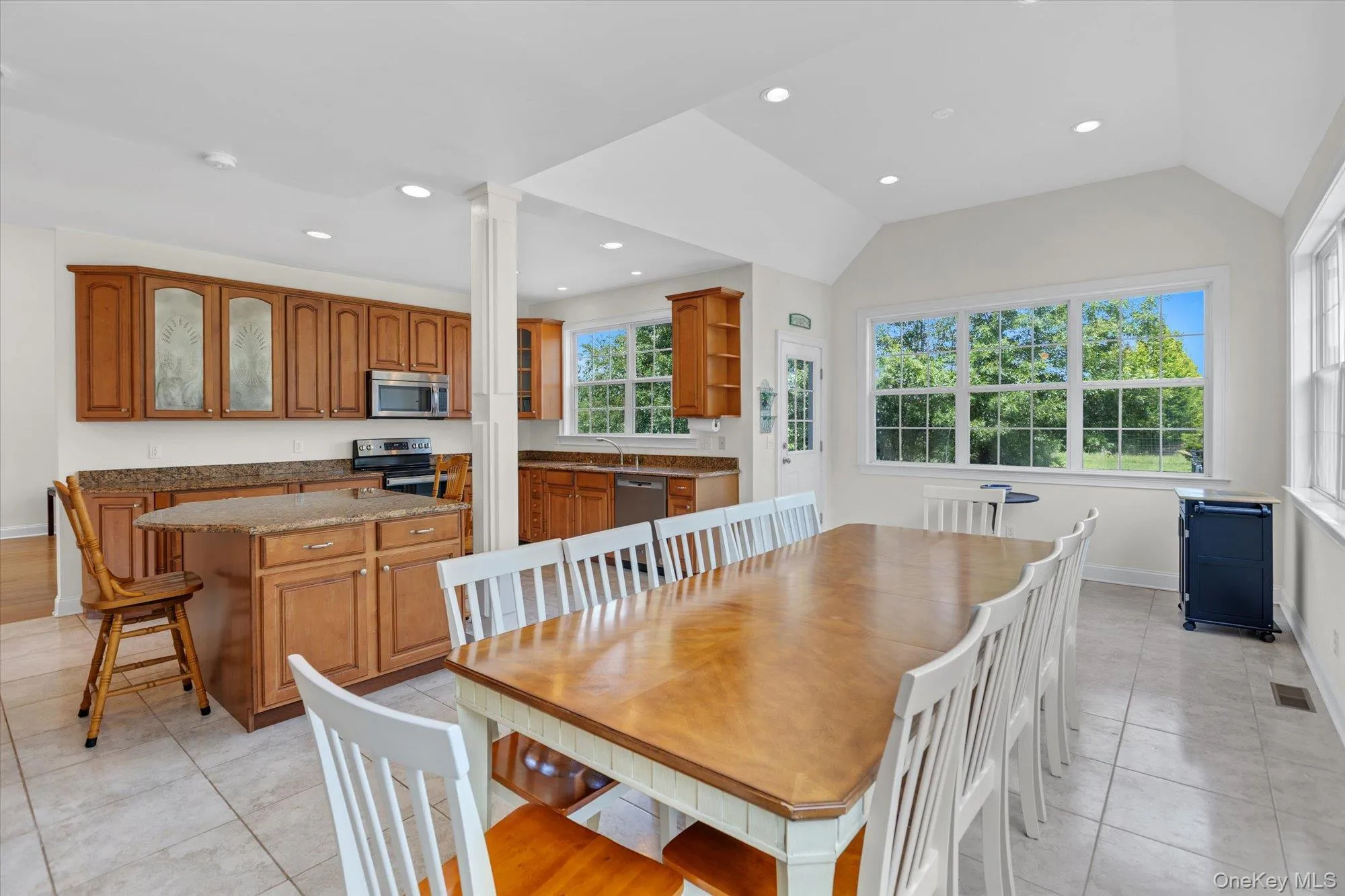 Expansive kitchen and dining area featuring wood cabinetry, stainless steel appliances, a kitchen island with seating, and tile flooring Expansive kitchen and dining area featuring wood cabinetry, stainless steel appliances, a kitchen island with seating, and tile flooring