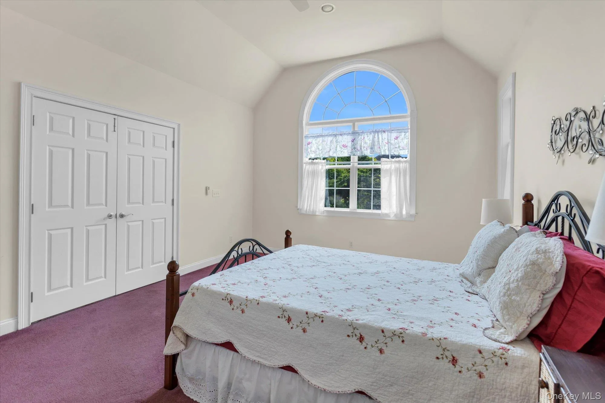 Bright bedroom suite featuring an arched transom window with plantation shutters, vaulted ceiling, wood-finish closet doors Bright bedroom suite featuring an arched transom window with plantation shutters, vaulted ceiling, wood-finish closet doors