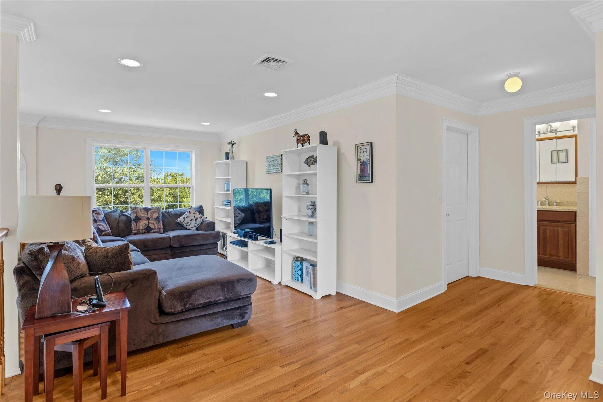 Bright, open living area showcasing hardwood flooring throughout, abundant natural light from large windows, white cabinetry with shelving and media storage, and recessed ceiling lighting Bright, open living area showcasing hardwood flooring throughout, abundant natural light from large windows, white cabinetry with shelving and media storage, and recessed ceiling lighting