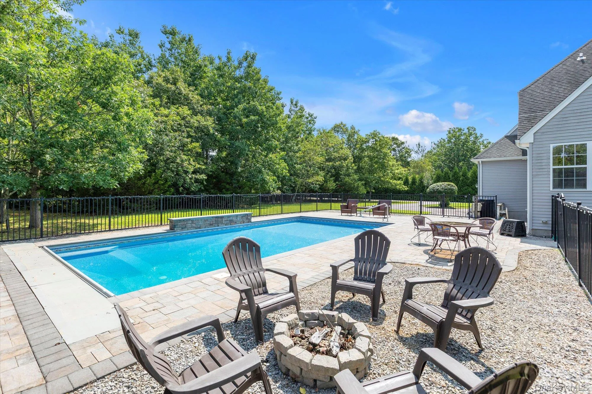 In-ground swimming pool with stone coping, paver patio, stone fire pit, and black fencing In-ground swimming pool with stone coping, paver patio, stone fire pit, and black fencing