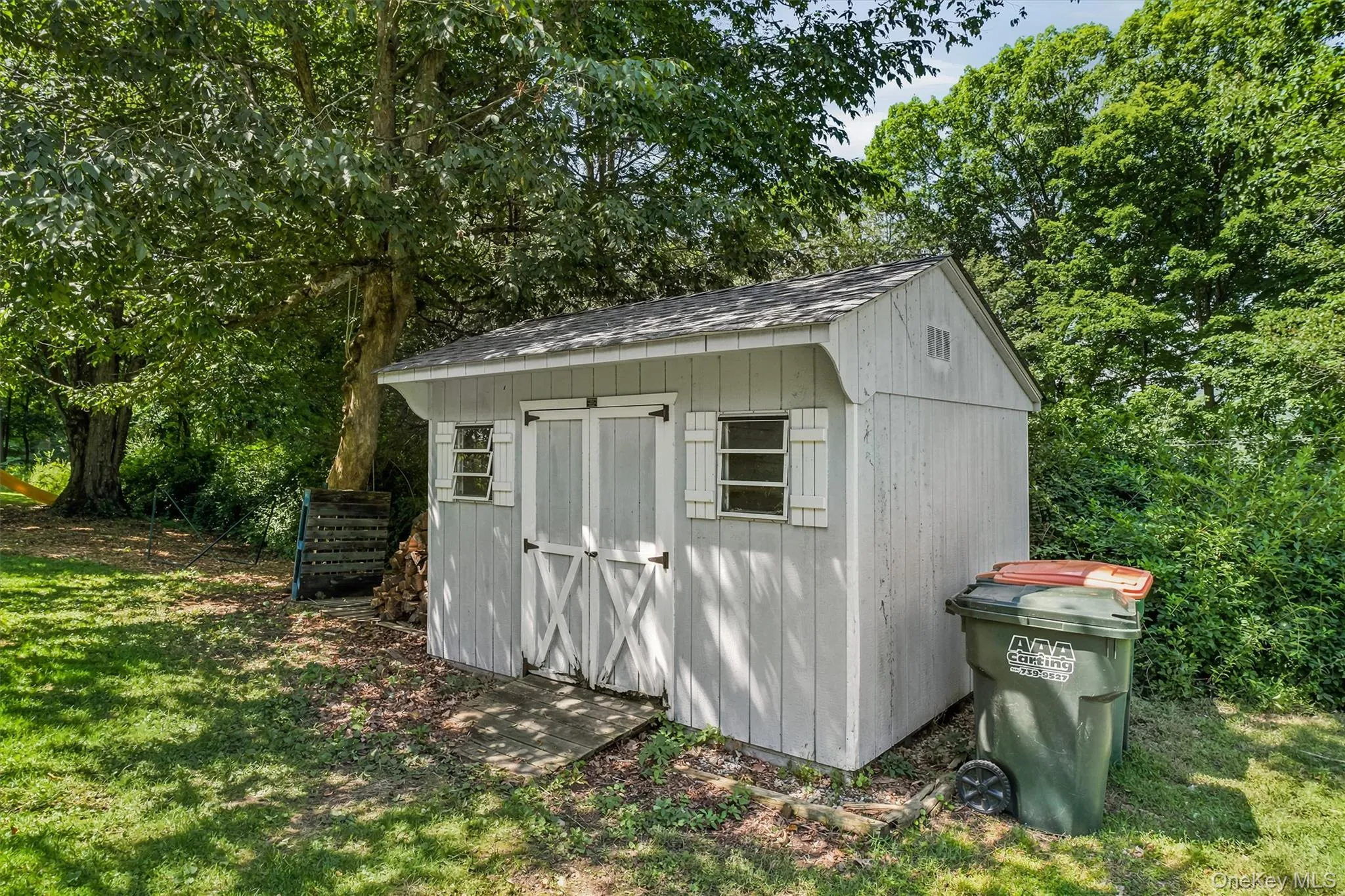Detached storage shed featuring wood paneling, gable roof, double barn doors, and two windows with shutters Detached storage shed featuring wood paneling, gable roof, double barn doors, and two windows with shutters