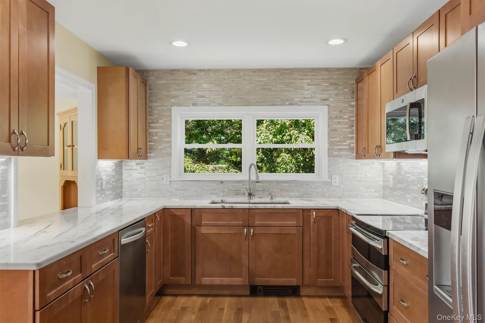 U-shaped kitchen with wood-finish cabinetry, stainless steel appliances, white countertops, and a full tile backsplash U-shaped kitchen with wood-finish cabinetry, stainless steel appliances, white countertops, and a full tile backsplash