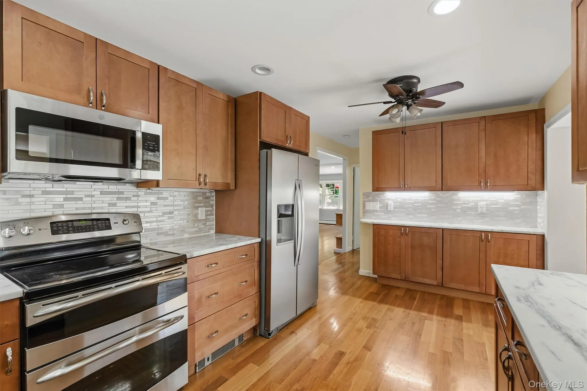 Kitchen featuring wood-finish flooring, stainless steel appliances, marble-look countertops, subway tile backsplash, and wood cabinetry Kitchen featuring wood-finish flooring, stainless steel appliances, marble-look countertops, subway tile backsplash, and wood cabinetry