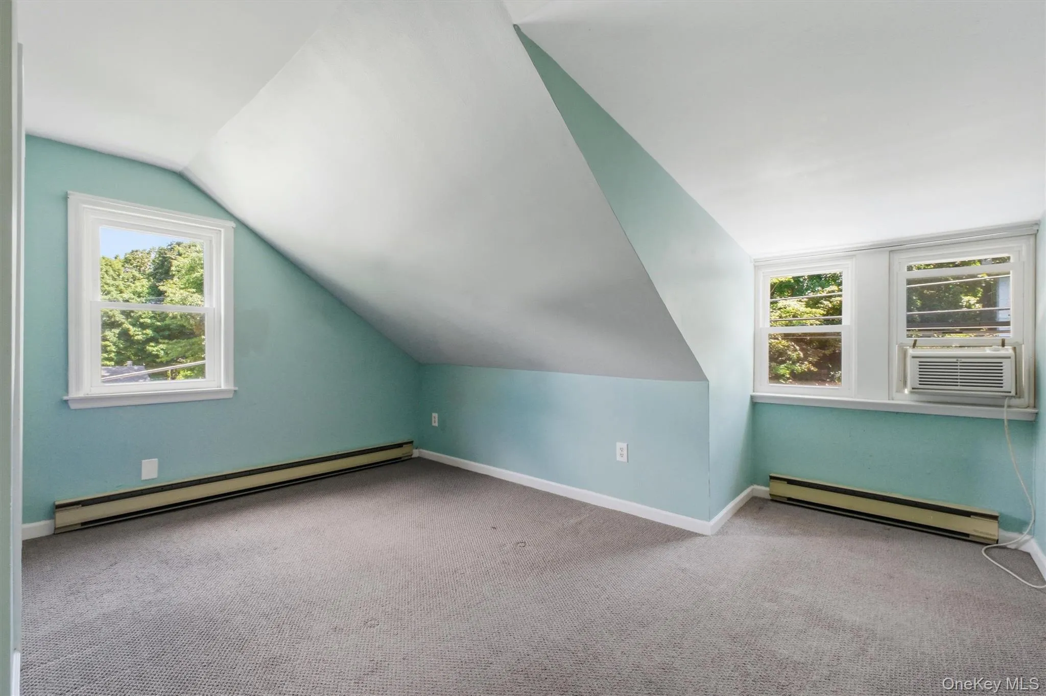 Carpeted bedroom featuring a sloped ceiling, two windows with white trim, and baseboard heating Carpeted bedroom featuring a sloped ceiling, two windows with white trim, and baseboard heating