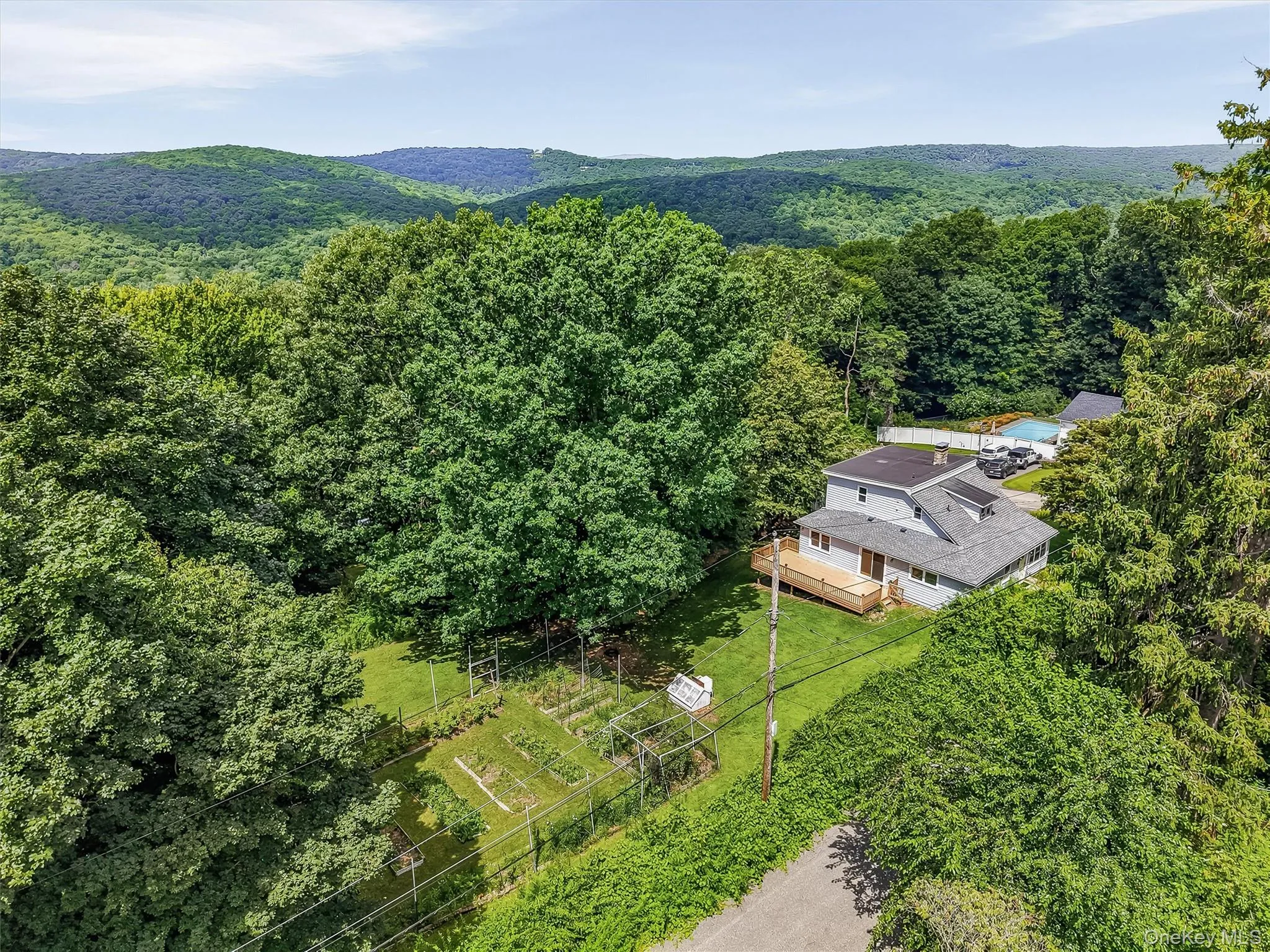 Home nestled among mature trees, featuring a light gray exterior, a multi-level roofline, and an expansive wooden deck Home nestled among mature trees, featuring a light gray exterior, a multi-level roofline, and an expansive wooden deck