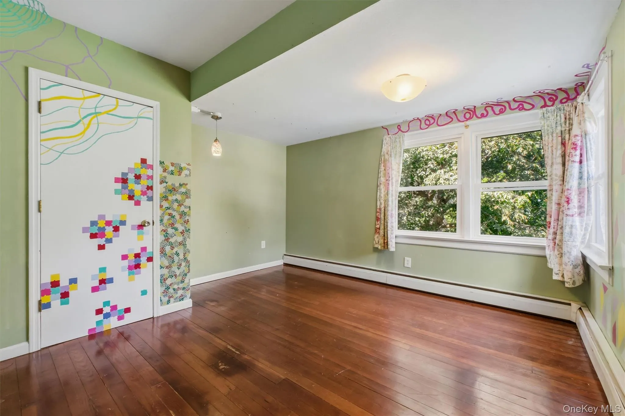 Room featuring wood-finish flooring, light green painted walls, and a ceiling-mounted light fixture Room featuring wood-finish flooring, light green painted walls, and a ceiling-mounted light fixture