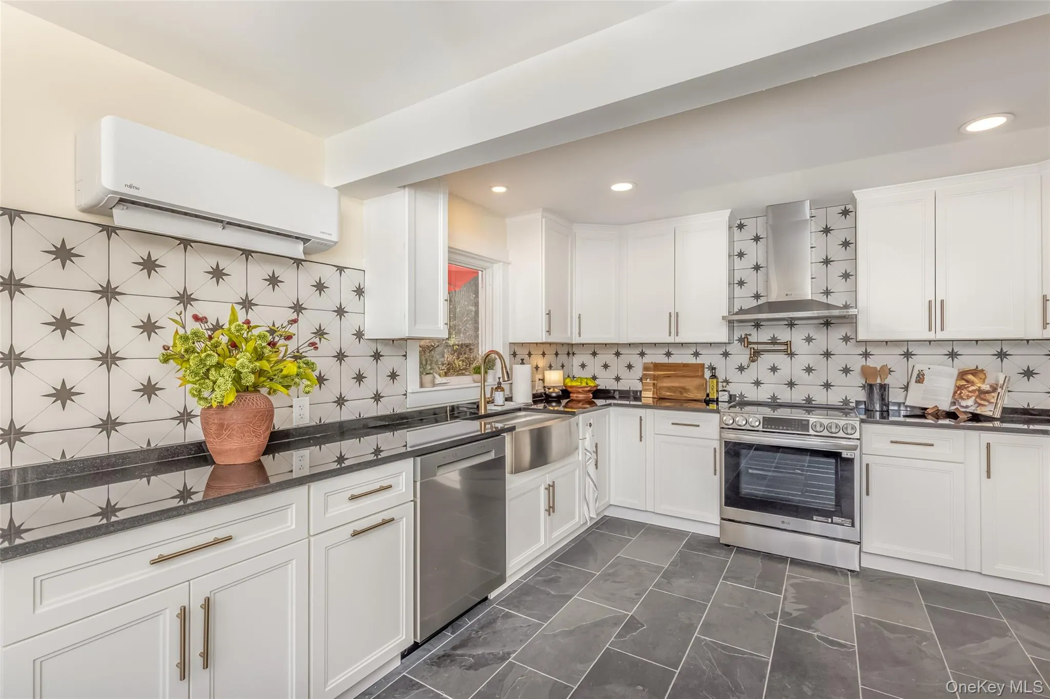 Kitchen featuring a wall mounted AC, white cabinets, wall chimney range hood, and appliances with stainless steel finishes Kitchen featuring a wall mounted AC, white cabinets, wall chimney range hood, and appliances with stainless steel finishes