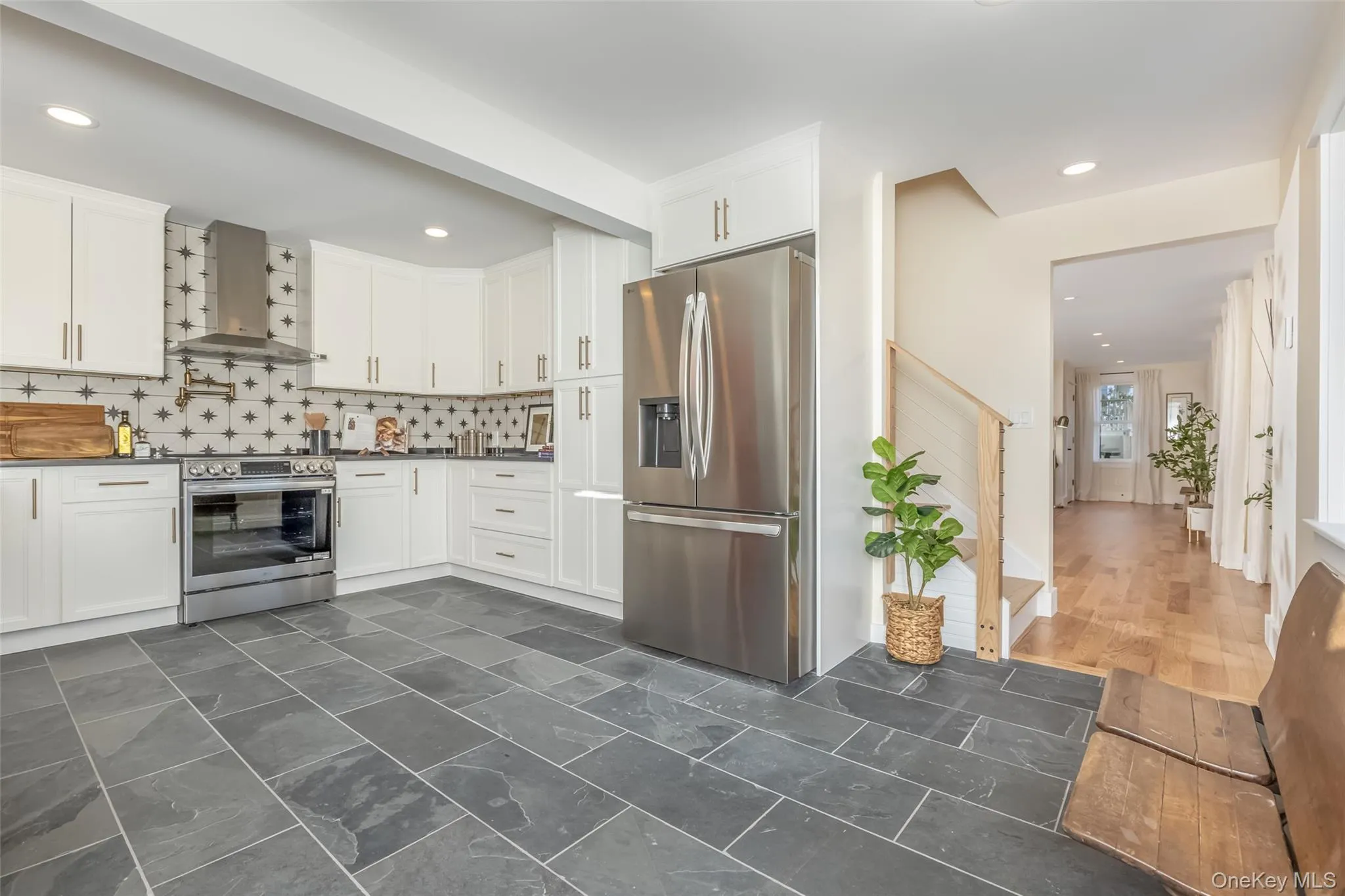 Kitchen featuring tasteful backsplash, white cabinets, wall chimney exhaust hood, and appliances with stainless steel finishes Kitchen featuring tasteful backsplash, white cabinets, wall chimney exhaust hood, and appliances with stainless steel finishes