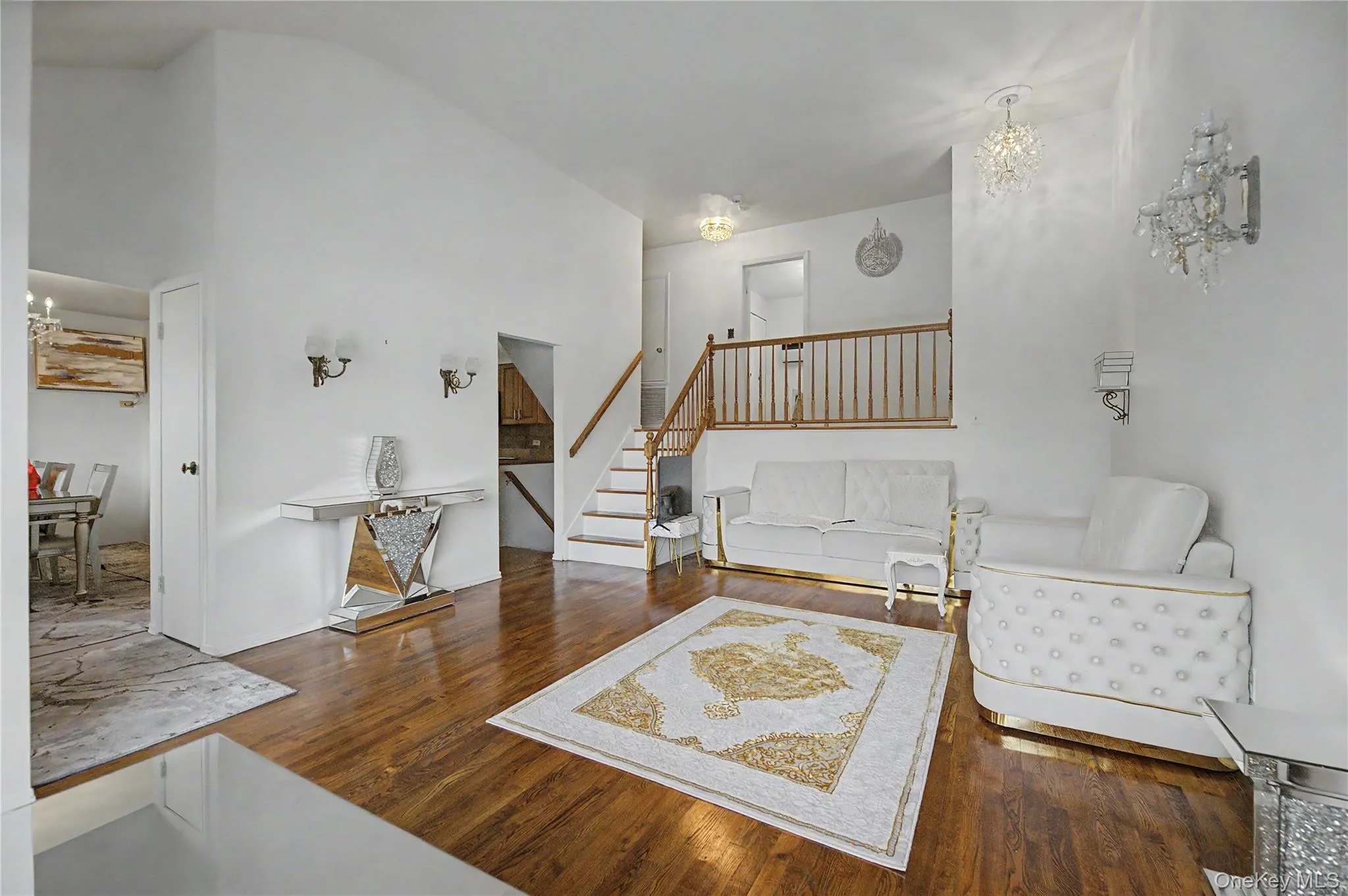 Open-concept living area featuring hardwood flooring, a two-story ceiling, a staircase with a wood railing, and an entryway with wall sconces Open-concept living area featuring hardwood flooring, a two-story ceiling, a staircase with a wood railing, and an entryway with wall sconces
