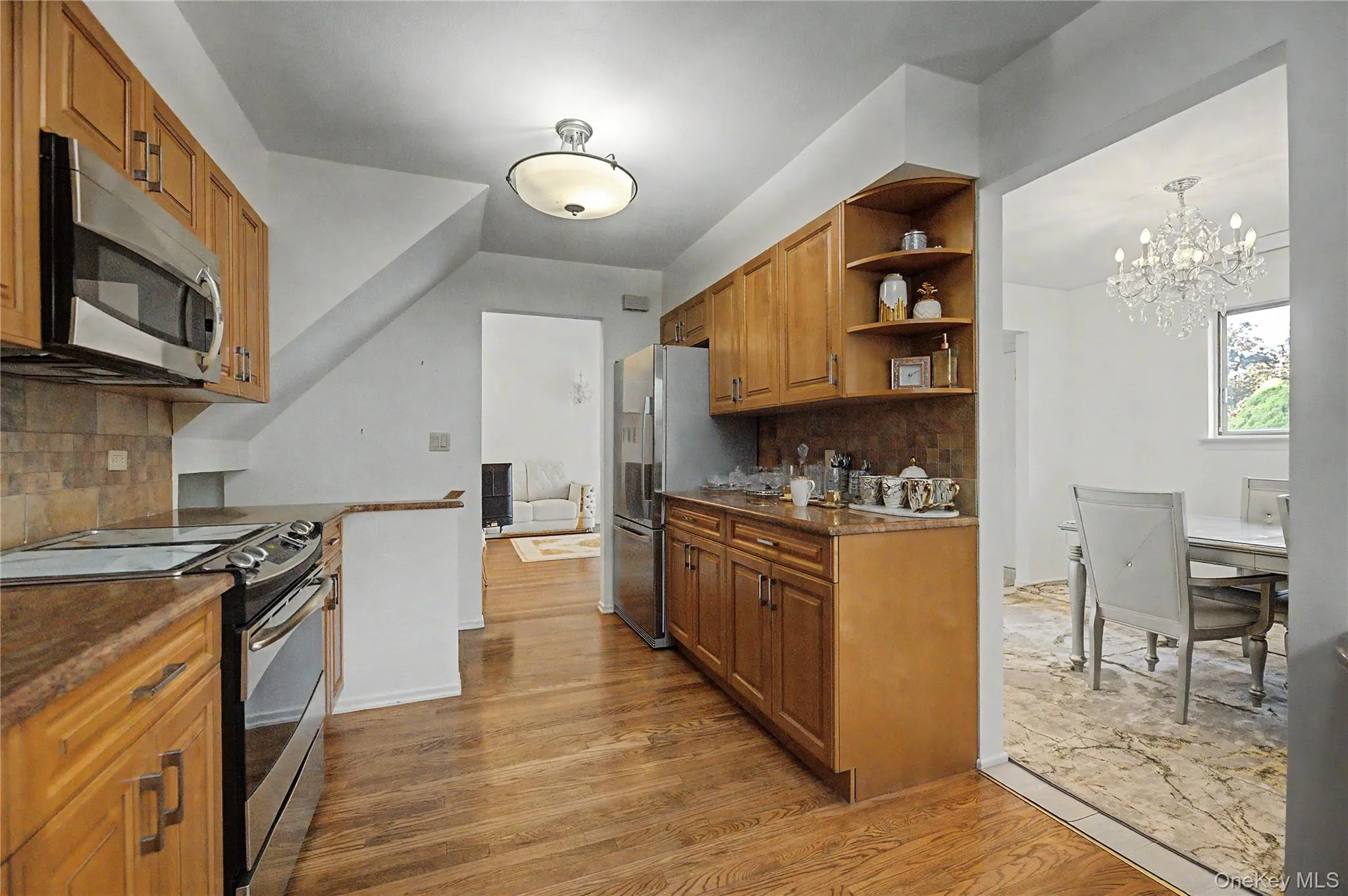 Kitchen featuring wood-finish flooring, natural wood cabinetry, stainless steel appliances, and a tiled backsplash Kitchen featuring wood-finish flooring, natural wood cabinetry, stainless steel appliances, and a tiled backsplash