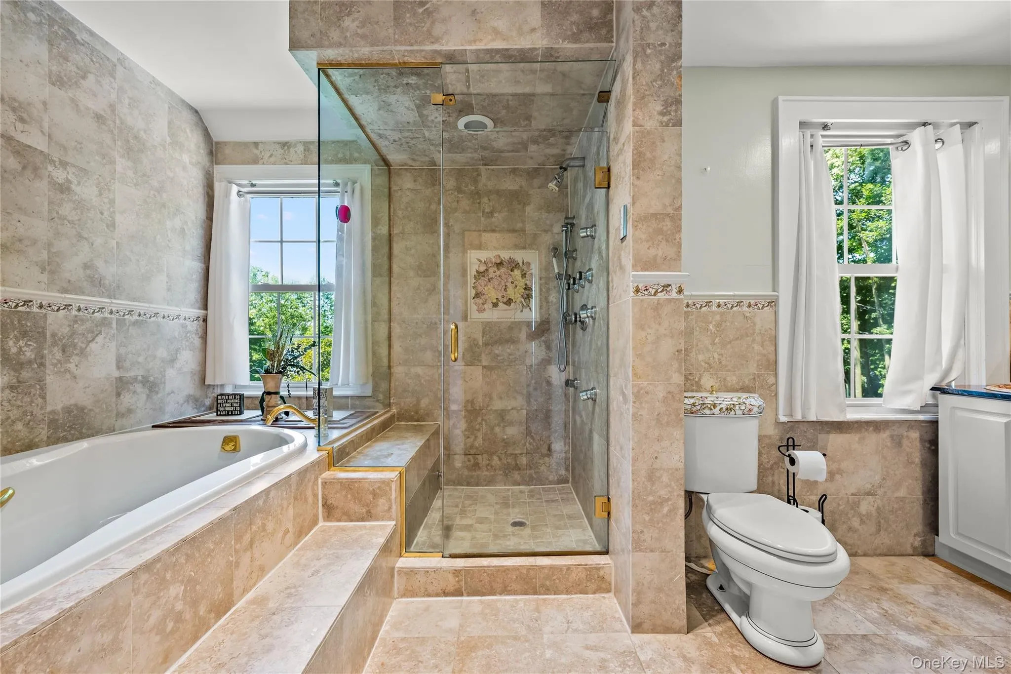 The ensuite bath blends timeless elegance with modern comfort, featuring warm natural stone, classic detailing, and beautifully updated fixtures. A generous glass-enclosed shower, deep soaking tub, and refined finishes create a serene retreat The ensuite bath blends timeless elegance with modern comfort, featuring warm natural stone, classic detailing, and beautifully updated fixtures. A generous glass-enclosed shower, deep soaking tub, and refined finishes create a serene retreat
