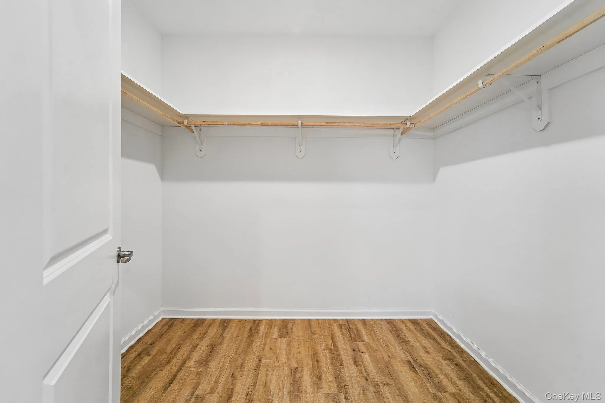 Primary Bedroom Walk-in closet featuring wood-finish flooring, white baseboards, and built-in shelving with hanging rods Primary Bedroom Walk-in closet featuring wood-finish flooring, white baseboards, and built-in shelving with hanging rods