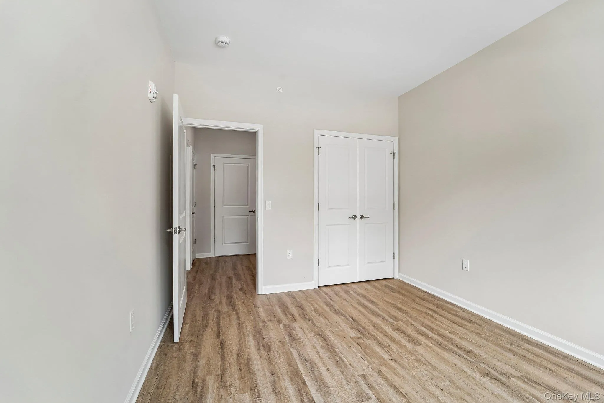 Room featuring wood-finish flooring, light neutral wall paint, and white baseboards Room featuring wood-finish flooring, light neutral wall paint, and white baseboards