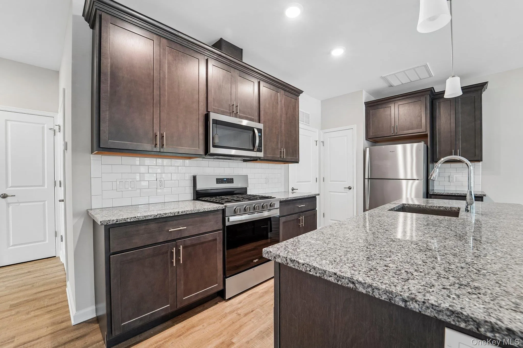Modern kitchen featuring rich wood cabinetry, granite countertops, stainless steel appliances, a gas range, subway-tile backsplash, and a large center island with sink and seating. Modern kitchen featuring rich wood cabinetry, granite countertops, stainless steel appliances, a gas range, subway-tile backsplash, and a large center island with sink and seating.