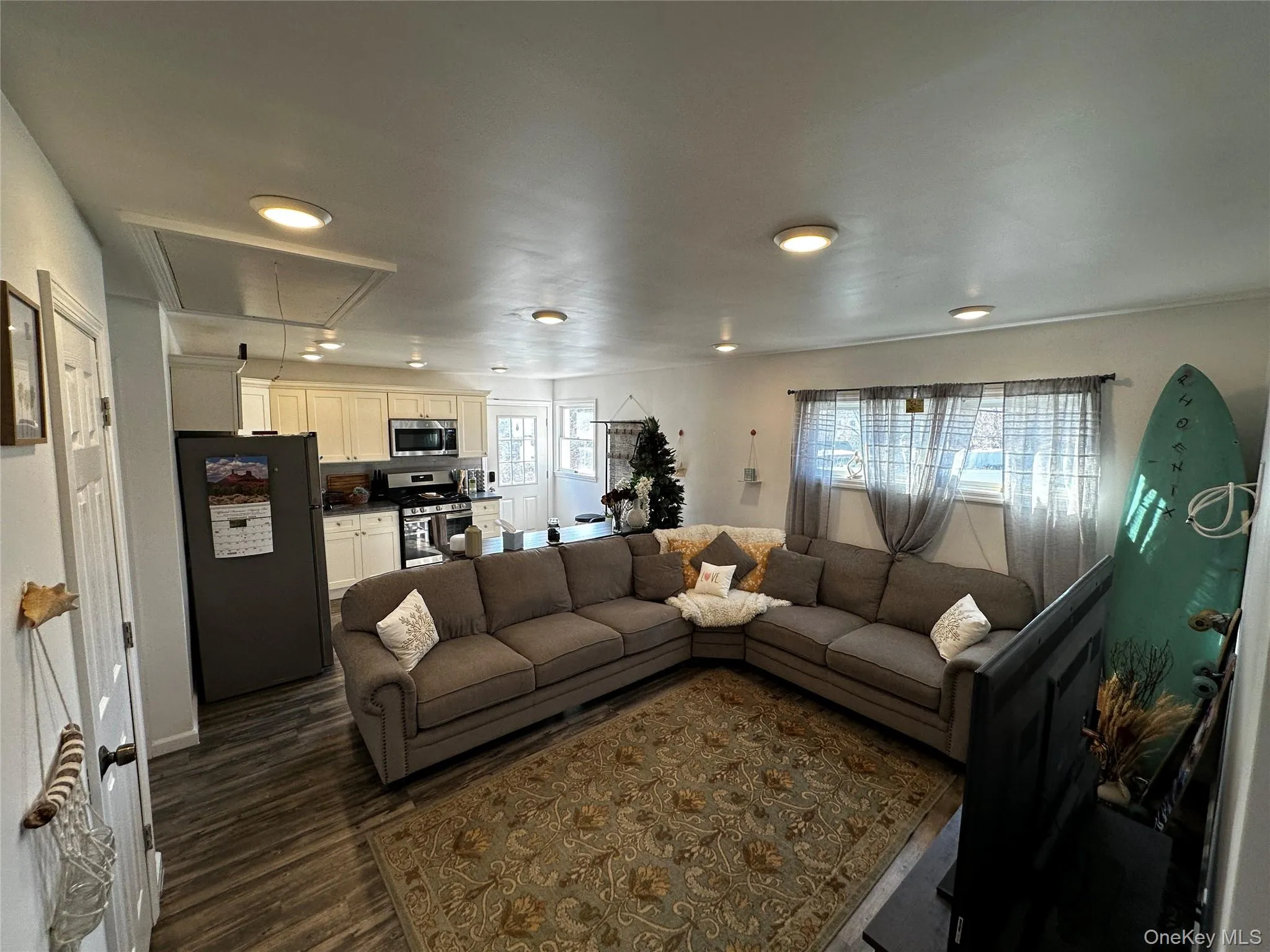 Open-concept living space featuring wood-finish flooring, recessed lighting, and a kitchen area with white cabinetry and stainless steel appliances Open-concept living space featuring wood-finish flooring, recessed lighting, and a kitchen area with white cabinetry and stainless steel appliances