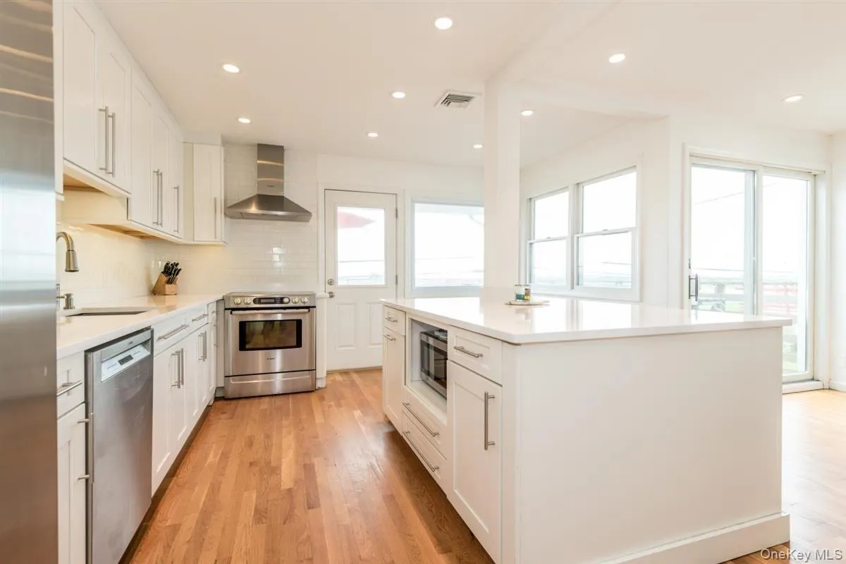 Modern kitchen featuring white cabinetry, stainless steel appliances, solid surface countertops, a center island with built-in microwave, and wood-finish flooring Modern kitchen featuring white cabinetry, stainless steel appliances, solid surface countertops, a center island with built-in microwave, and wood-finish flooring