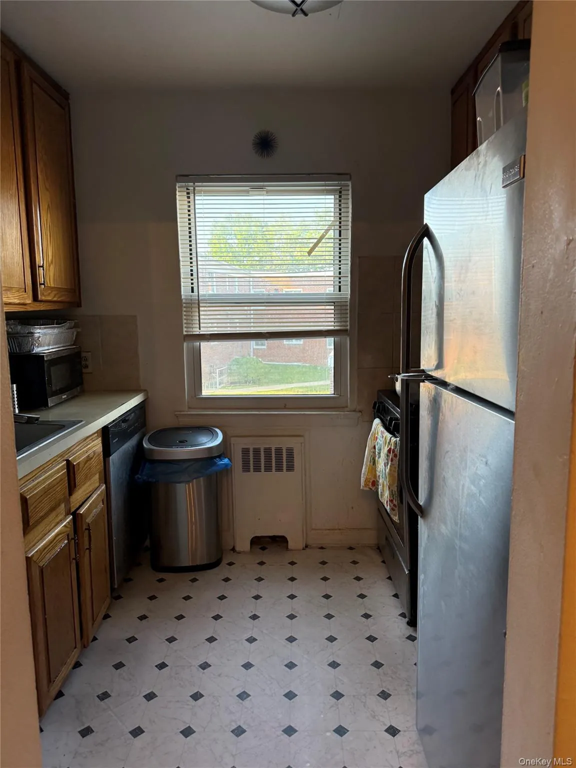 Compact kitchen featuring neutral-toned cabinetry, a window with blinds, and geometric pattern flooring Compact kitchen featuring neutral-toned cabinetry, a window with blinds, and geometric pattern flooring