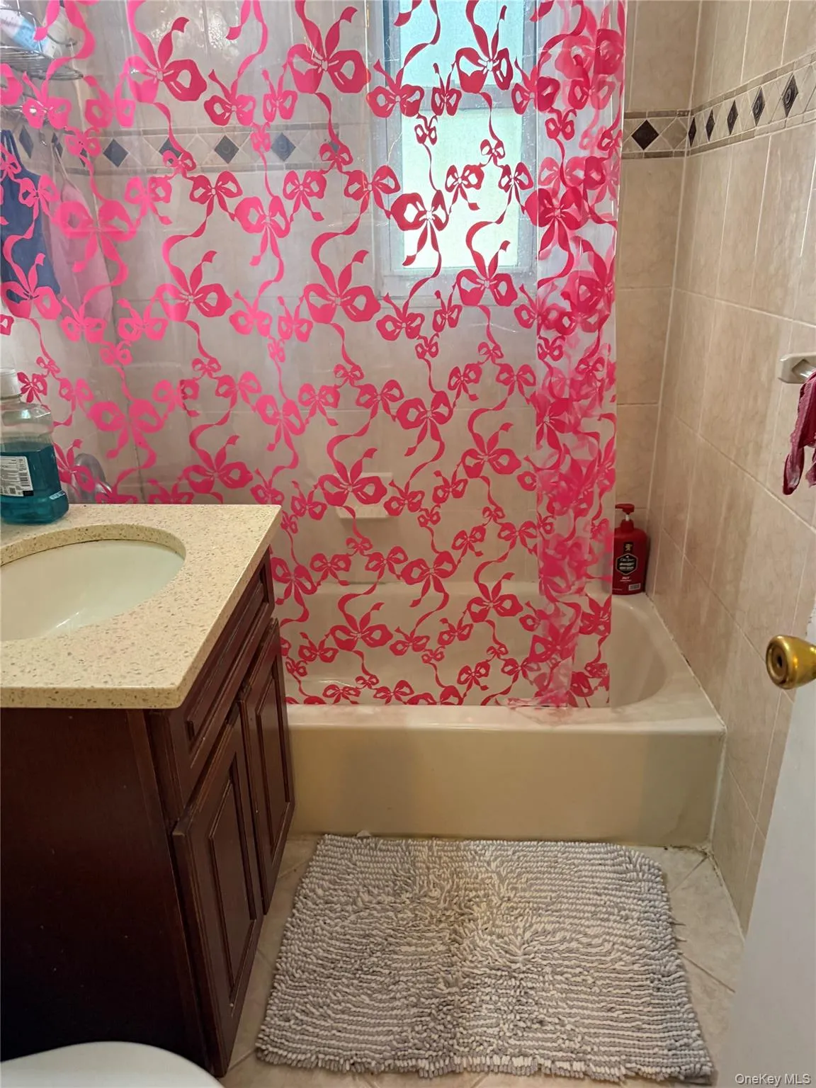 Bathroom featuring a built-in bathtub, a window, ceramic wall tiling with decorative accent, a vanity with a countertop, and a basin Bathroom featuring a built-in bathtub, a window, ceramic wall tiling with decorative accent, a vanity with a countertop, and a basin