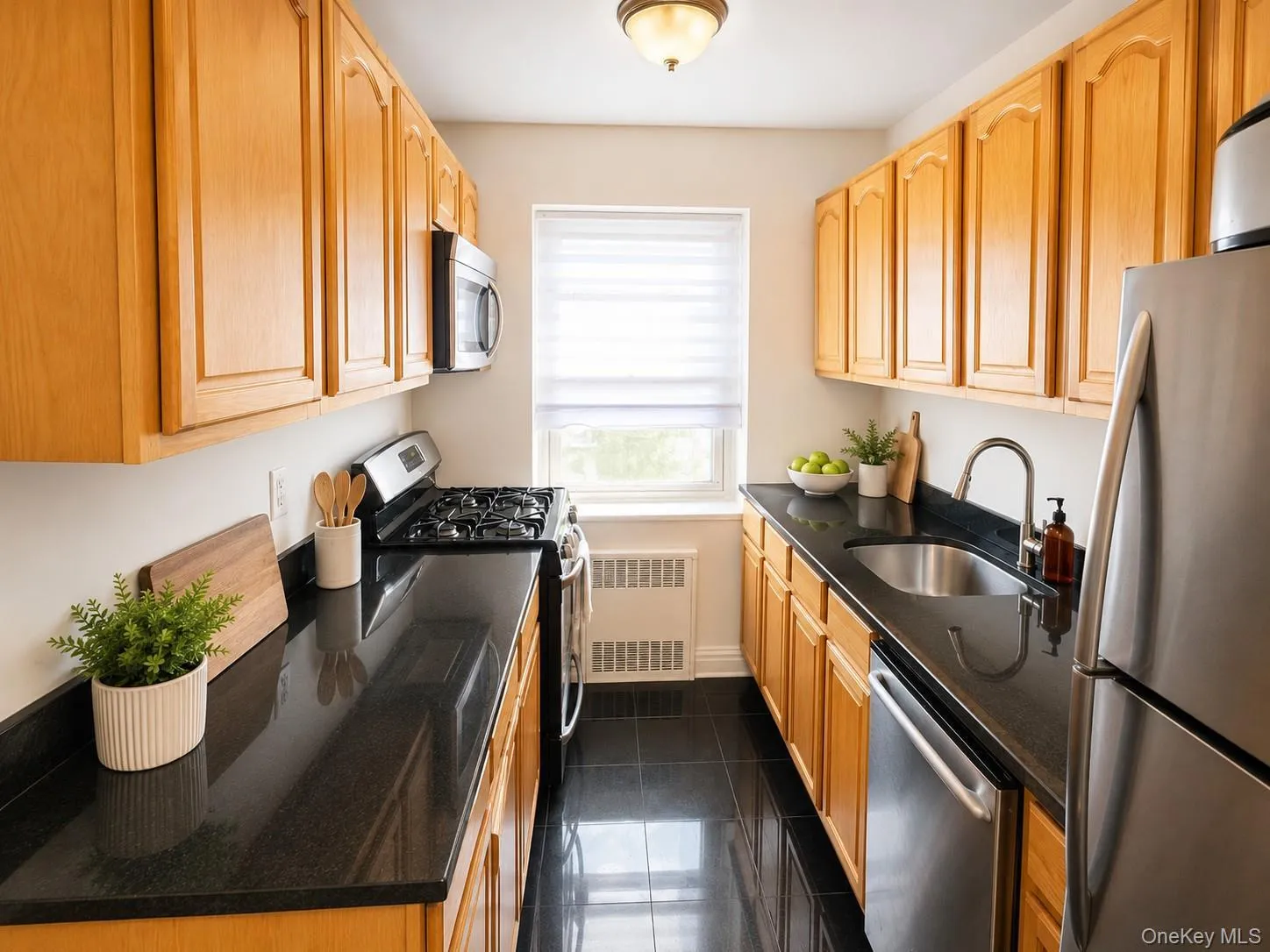Galley kitchen featuring natural wood cabinetry, black countertops, stainless steel appliances, and a window Galley kitchen featuring natural wood cabinetry, black countertops, stainless steel appliances, and a window