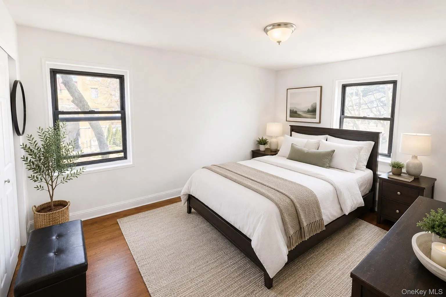 Bright room featuring two windows with black frames, wood-finish flooring, a ceiling-mounted light fixture, and white painted walls Bright room featuring two windows with black frames, wood-finish flooring, a ceiling-mounted light fixture, and white painted walls