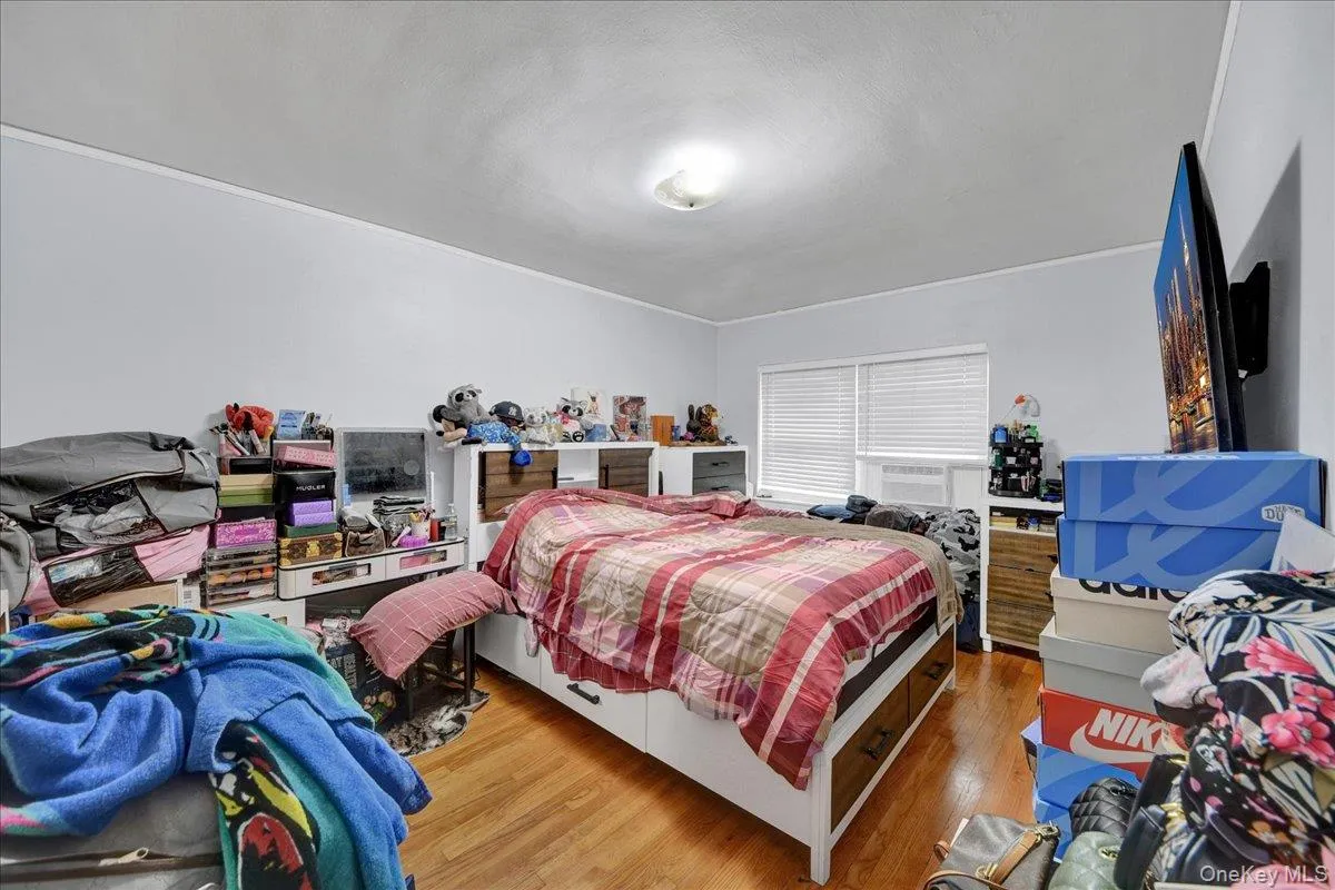 Bedroom featuring wood-finish flooring, light grey painted walls, white trim, and a window with blinds Bedroom featuring wood-finish flooring, light grey painted walls, white trim, and a window with blinds