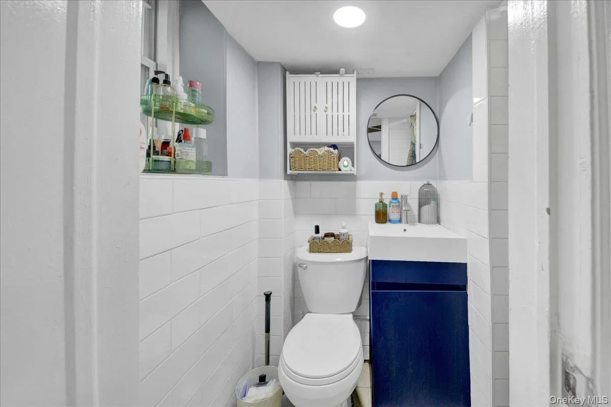Compact bathroom featuring white subway tile wainscoting and a modern wall-mounted vanity with a deep blue base and integrated sink Compact bathroom featuring white subway tile wainscoting and a modern wall-mounted vanity with a deep blue base and integrated sink