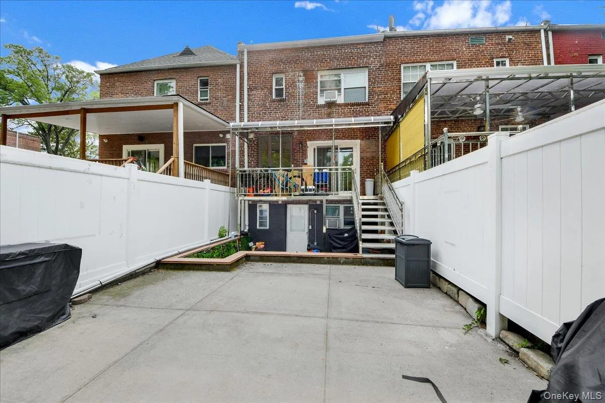 Paved patio area with a privacy fence, raised planter beds, a covered deck, and a second-story balcony with an awning Paved patio area with a privacy fence, raised planter beds, a covered deck, and a second-story balcony with an awning