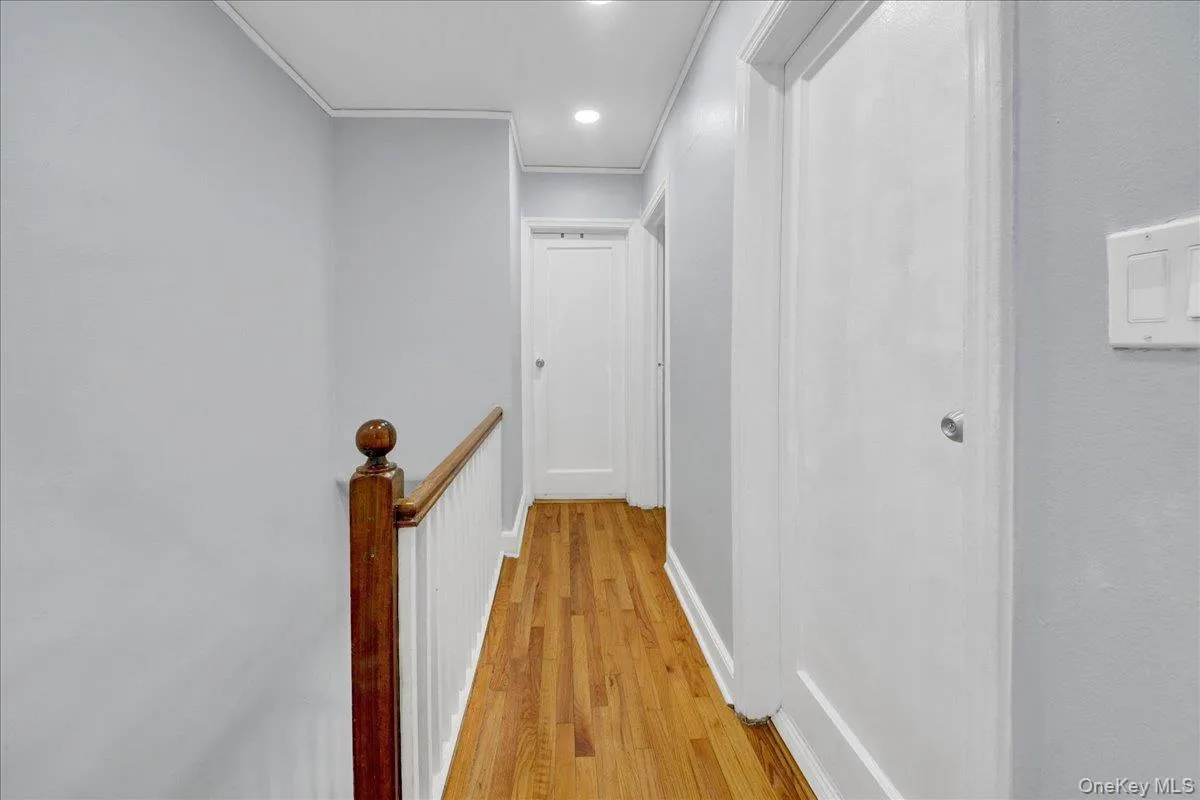 Light-filled hallway featuring wood-finish flooring, recessed lighting, white trim, and a classic wood banister Light-filled hallway featuring wood-finish flooring, recessed lighting, white trim, and a classic wood banister