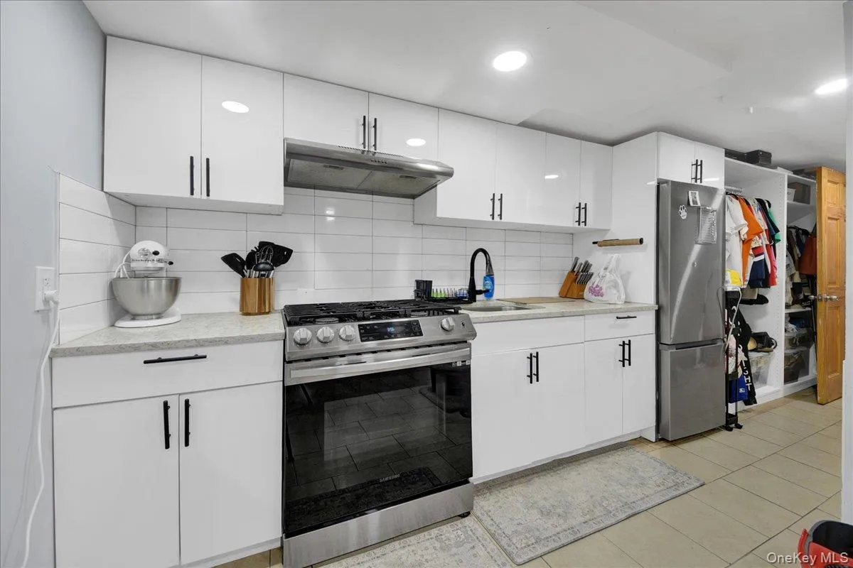 Kitchen featuring white high-gloss cabinetry, stainless steel appliances, a subway tile backsplash, and light-toned countertops Kitchen featuring white high-gloss cabinetry, stainless steel appliances, a subway tile backsplash, and light-toned countertops