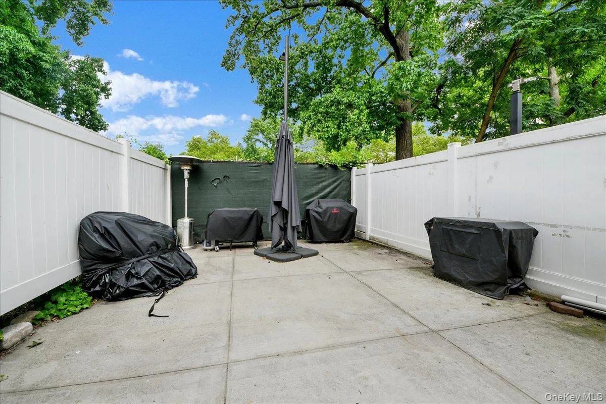 Concrete patio space featuring a perimeter fence, mature trees, and open sky Concrete patio space featuring a perimeter fence, mature trees, and open sky