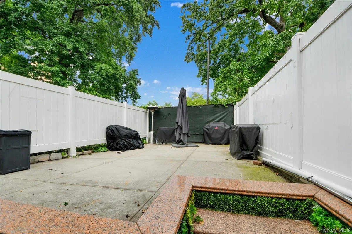 Paved outdoor patio area with white privacy fencing and mature perimeter trees Paved outdoor patio area with white privacy fencing and mature perimeter trees