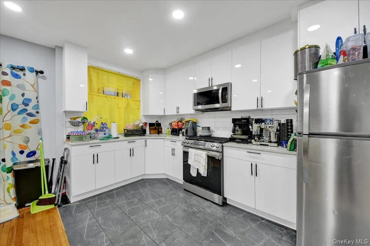 Modern kitchen featuring white flat-panel cabinetry, stainless steel appliances, white subway tile backsplash, and dark patterned floor tiles Modern kitchen featuring white flat-panel cabinetry, stainless steel appliances, white subway tile backsplash, and dark patterned floor tiles