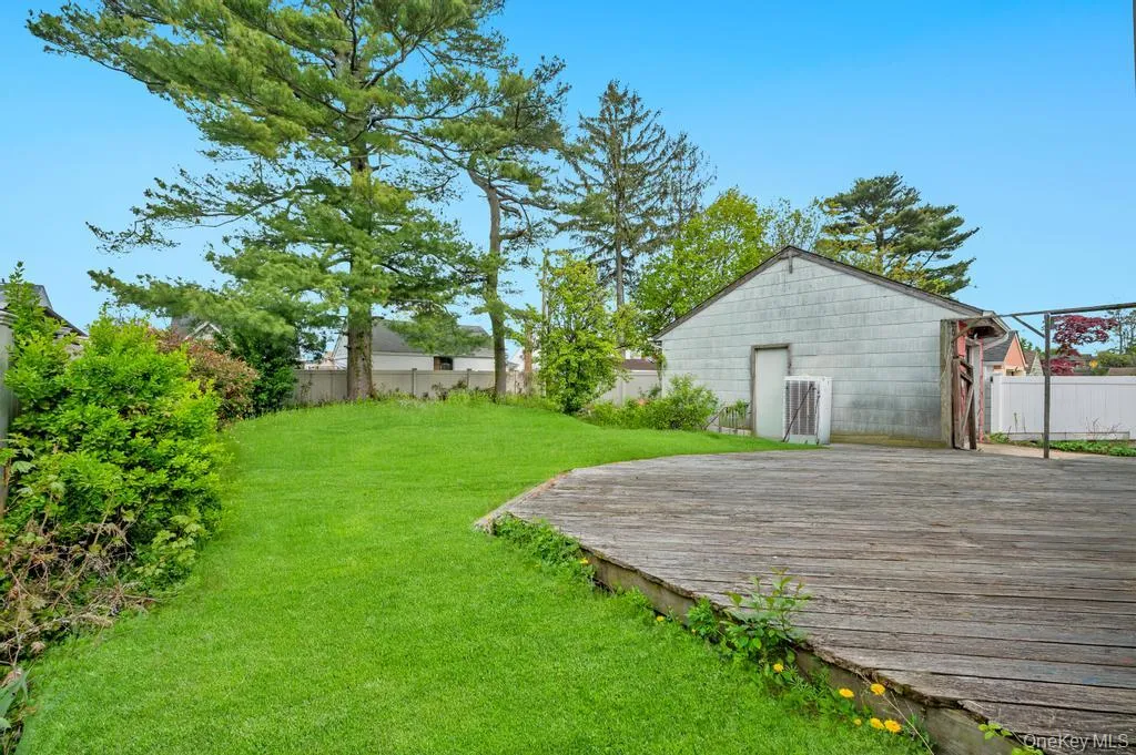 Spacious outdoor area featuring a wooden deck, a manicured lawn, established perimeter trees, and a detached structure with a side entrance Spacious outdoor area featuring a wooden deck, a manicured lawn, established perimeter trees, and a detached structure with a side entrance