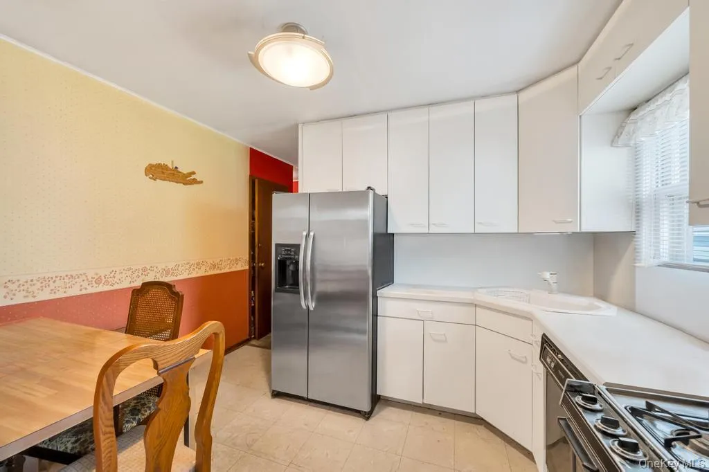 Kitchen featuring white cabinetry, solid surface countertops, stainless steel refrigerator, and built-in range Kitchen featuring white cabinetry, solid surface countertops, stainless steel refrigerator, and built-in range