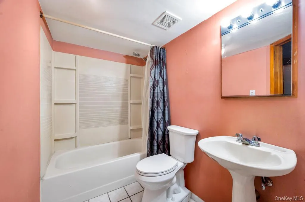 Bathroom featuring a white pedestal sink, toilet, and a combined tub and shower unit with a white surround Bathroom featuring a white pedestal sink, toilet, and a combined tub and shower unit with a white surround