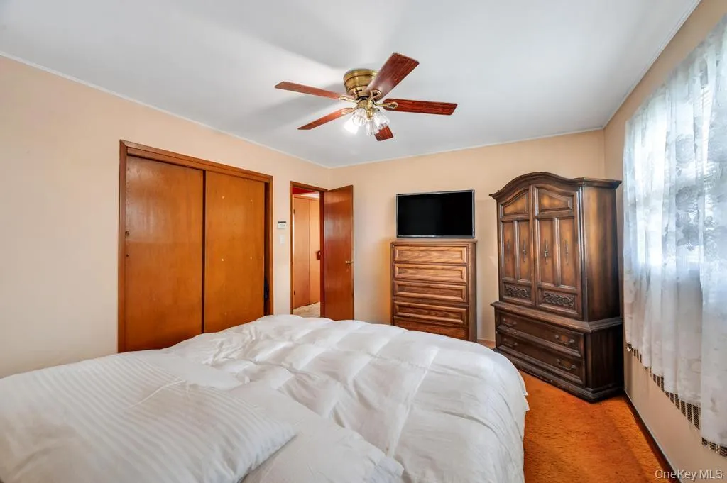 Bedroom featuring wood-finish sliding closet doors, a wood-finish ceiling fan with lighting, and a window with natural light Bedroom featuring wood-finish sliding closet doors, a wood-finish ceiling fan with lighting, and a window with natural light
