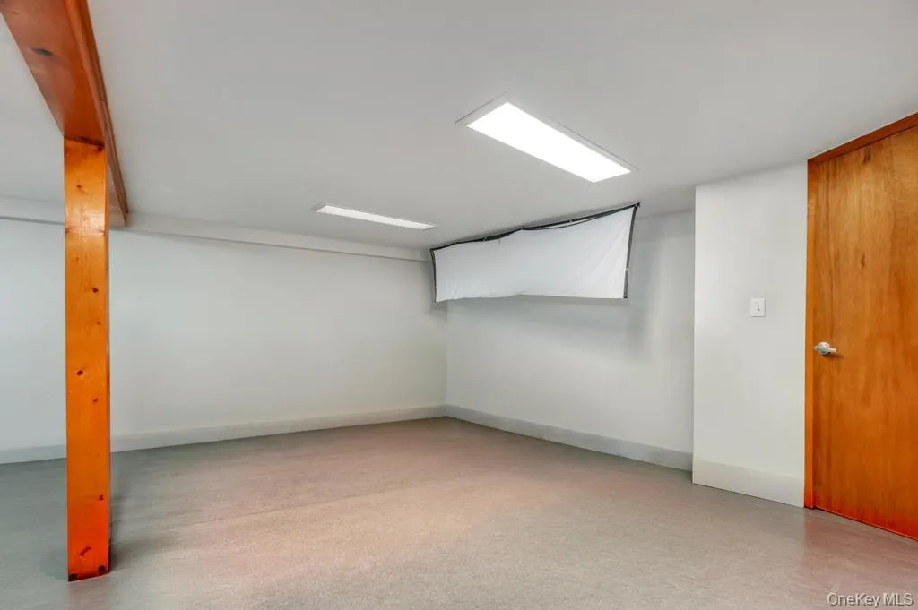 Spacious room featuring light-colored flooring, white walls, and a light-stained wood support beam Spacious room featuring light-colored flooring, white walls, and a light-stained wood support beam